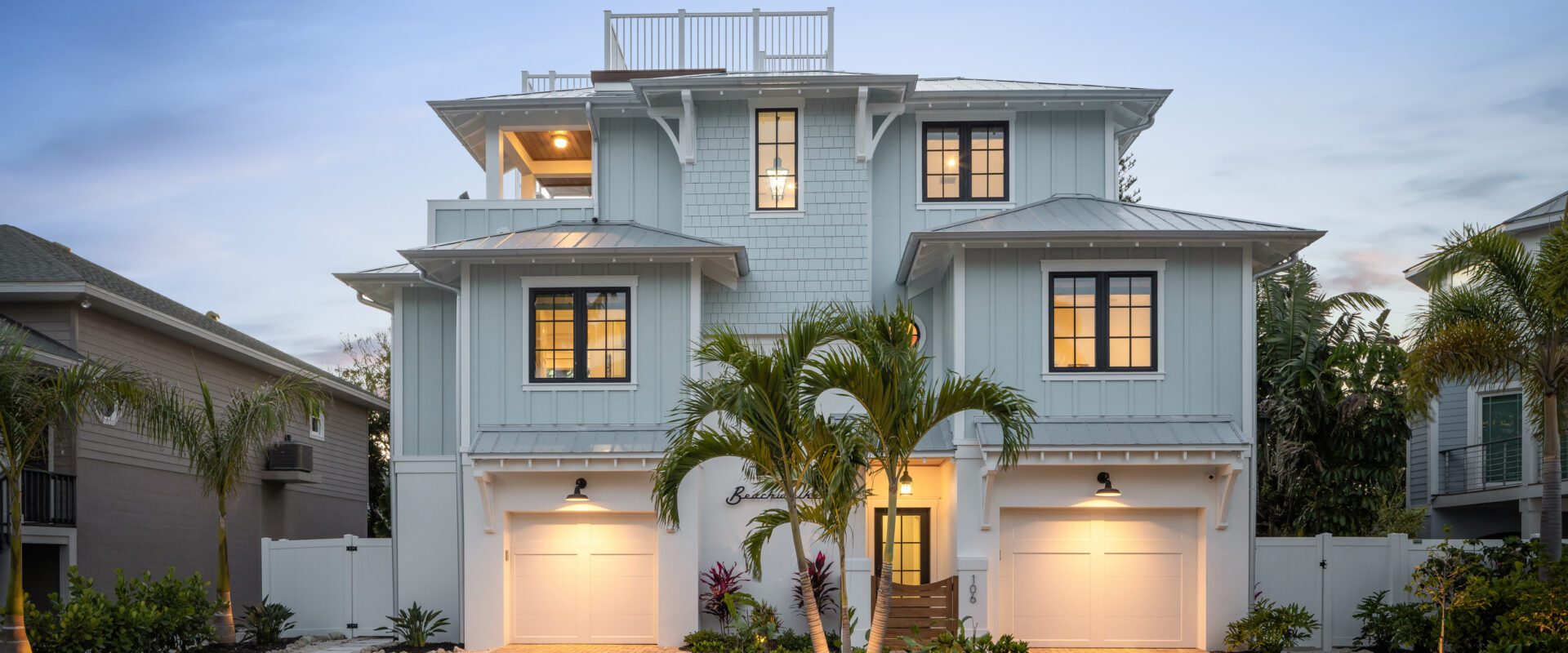 Beachwalker, a three-story blue-gray beach house with a rooftop deck, at dusk