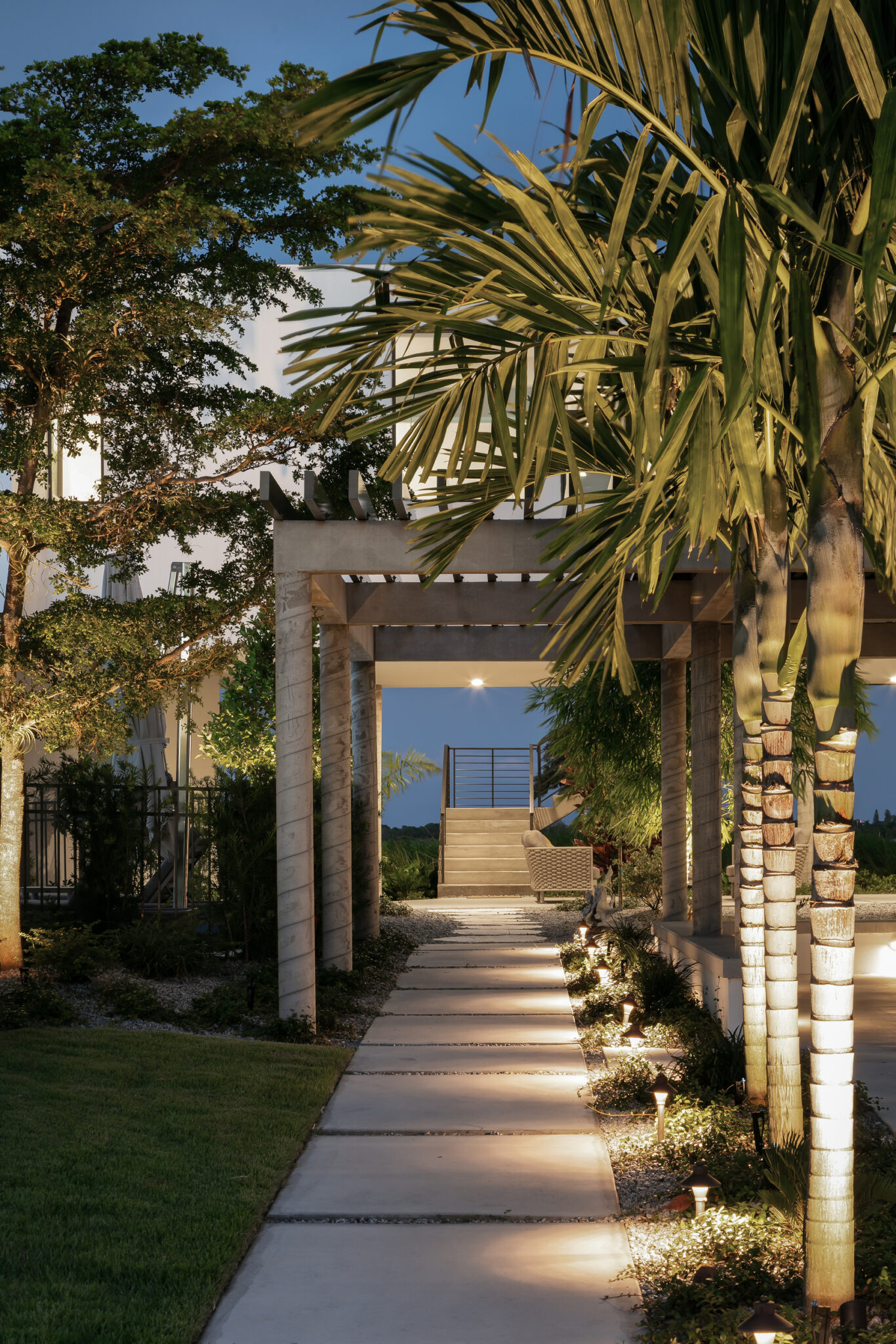Lit garden path under palms leading to the bay
