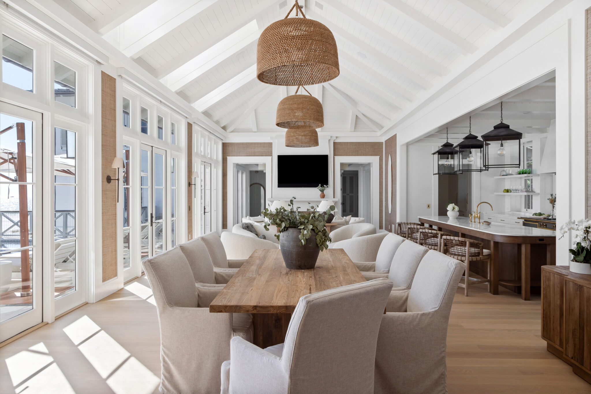 Dining table under a woven pendant, with the kitchen beyond