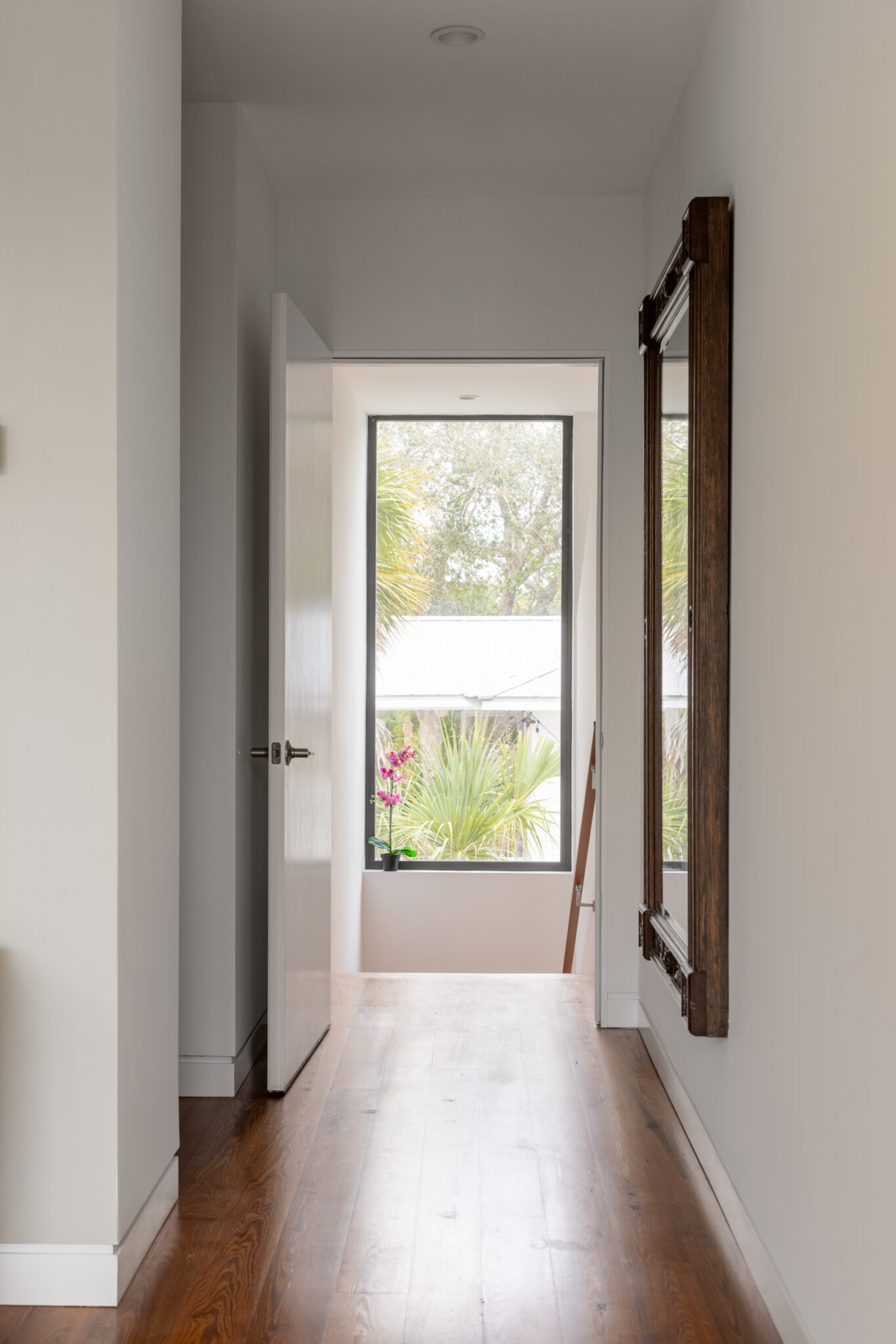 Hallway with wood floors and a tall window at the end