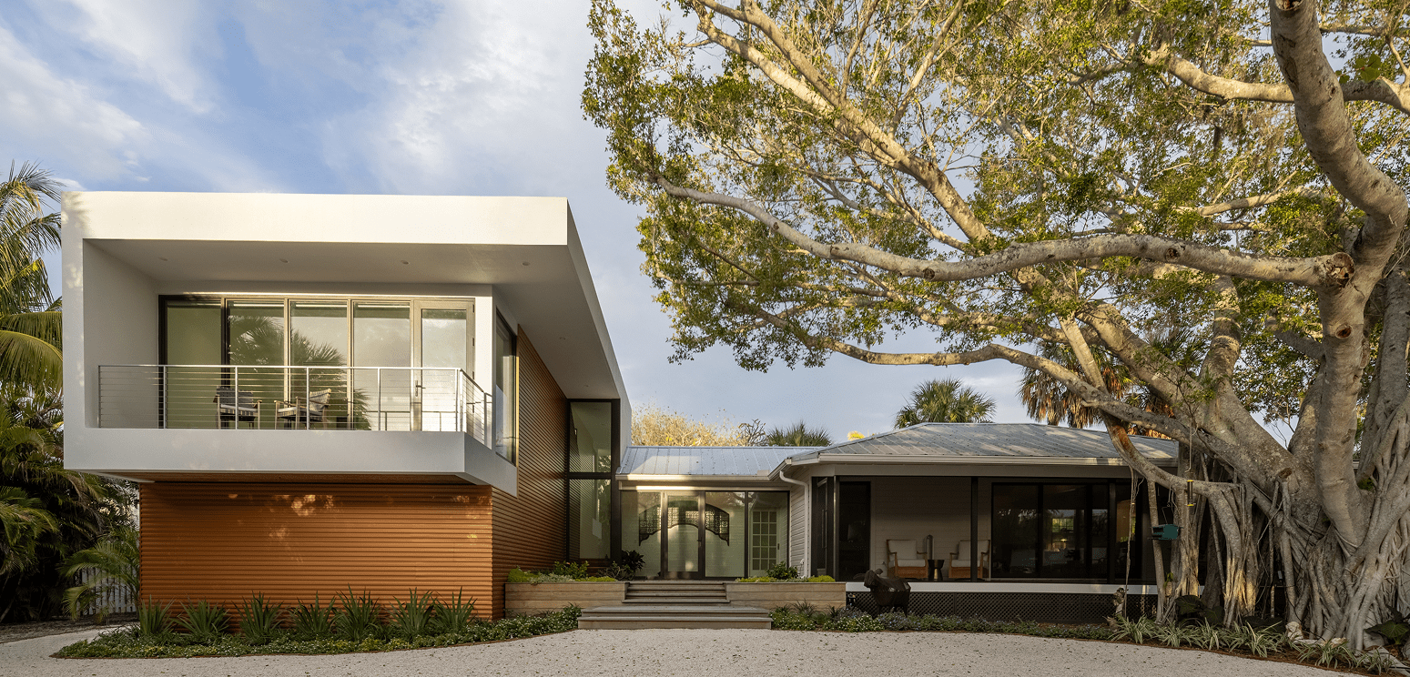 Schoolhouse Modern by day, the white cantilevered addition joined to the original schoolhouse beside a large shade tree