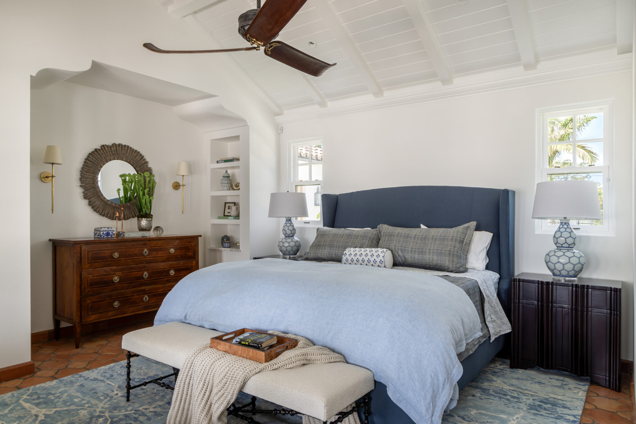 Bedroom with a navy headboard, round mirror and ceiling fan
