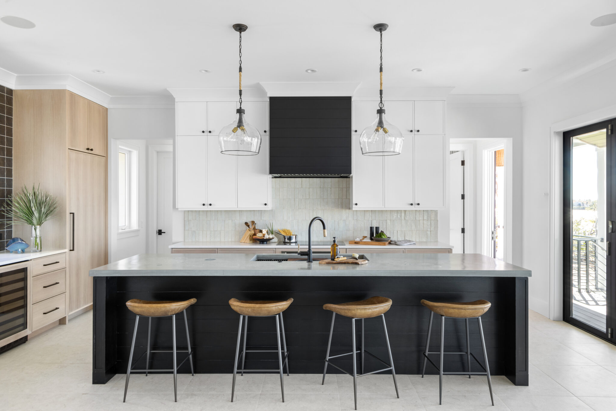 Kitchen island in black with wood stools and glass pendants