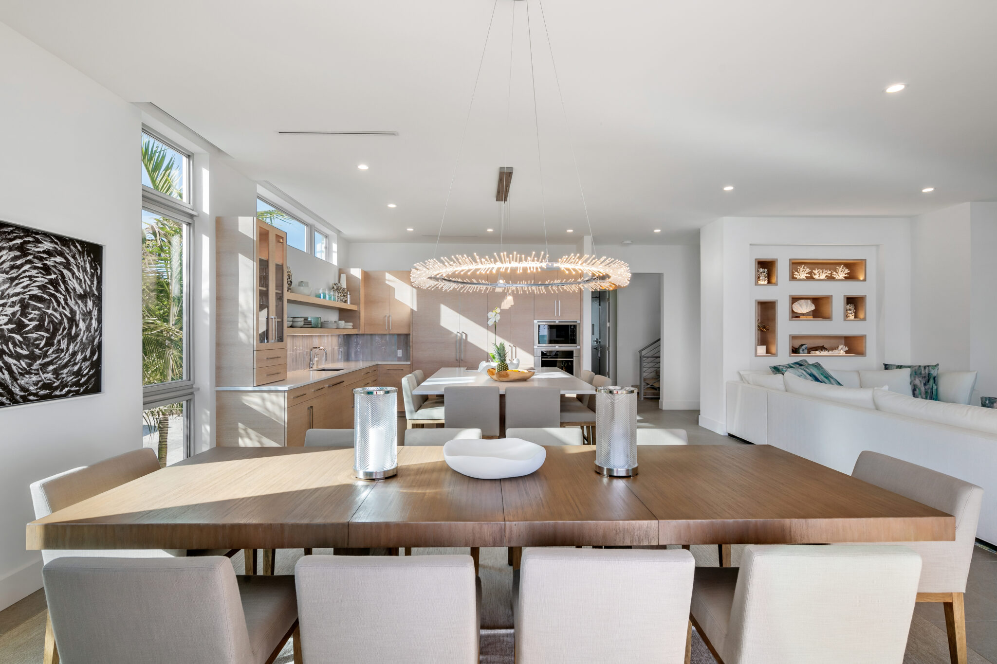 Dining table under a ring chandelier, open to the living room