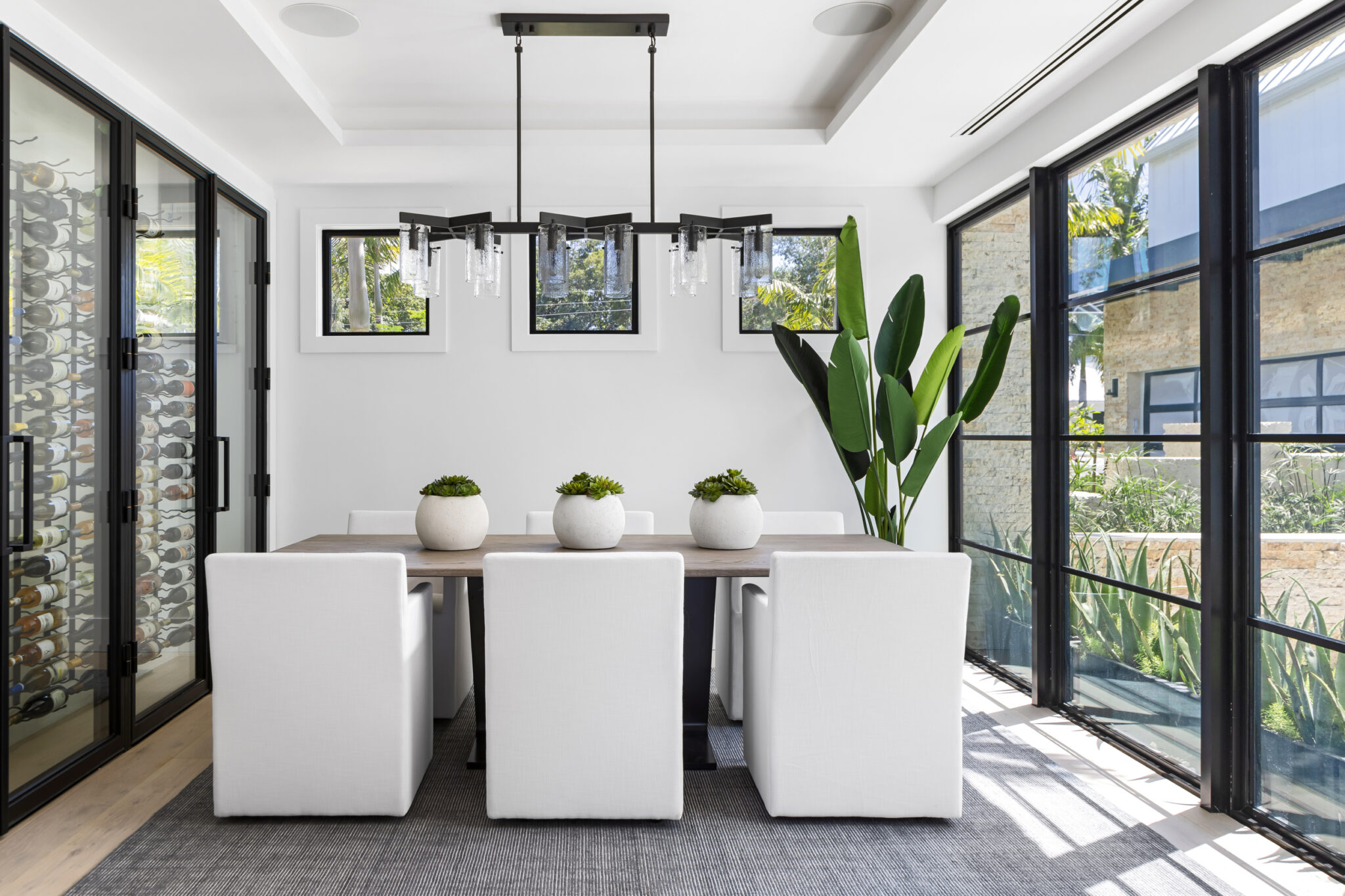 Dining room with white chairs and a glass wine wall beside steel windows
