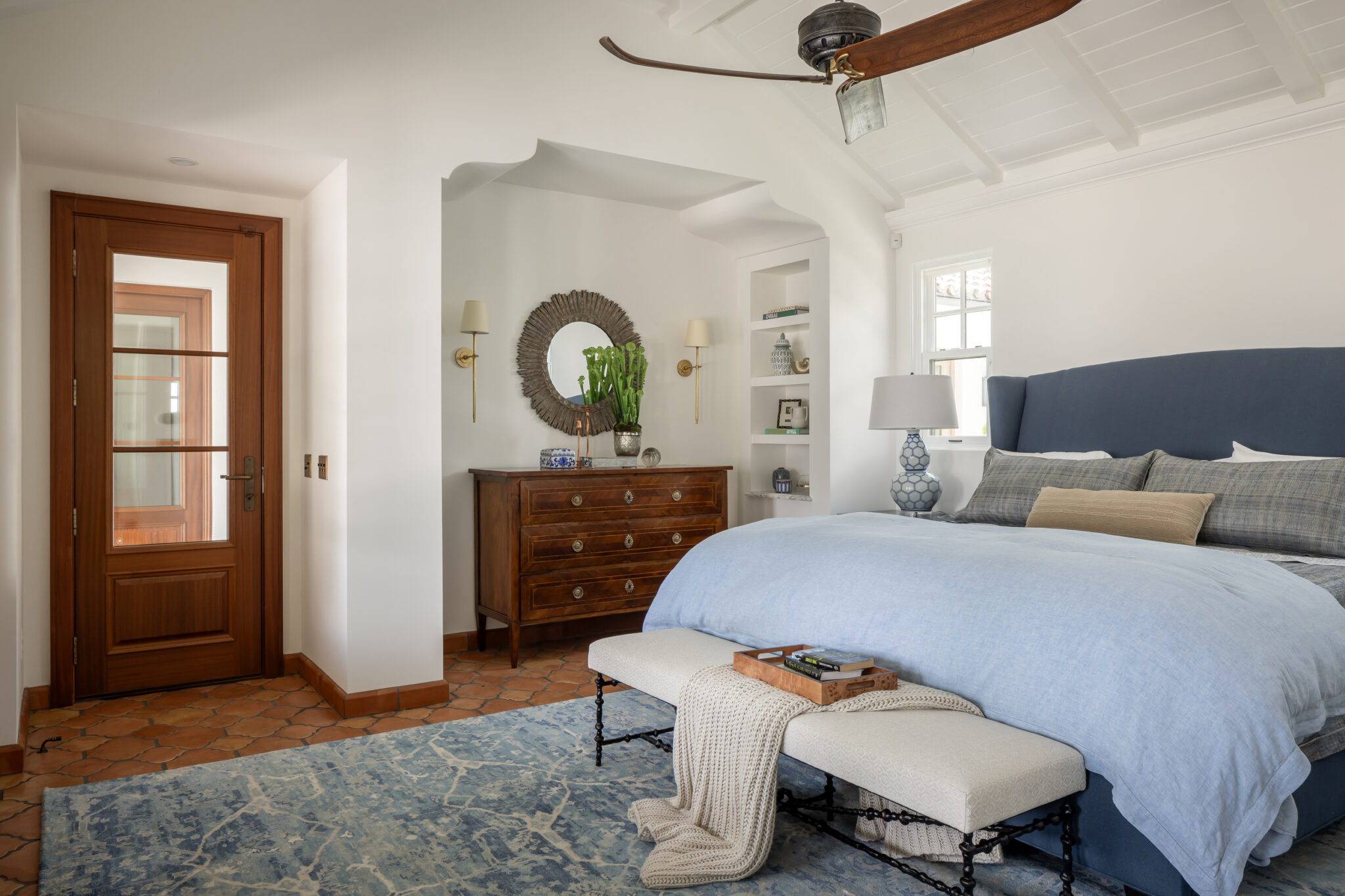 Bedroom with a wood door, round mirror and terracotta floor