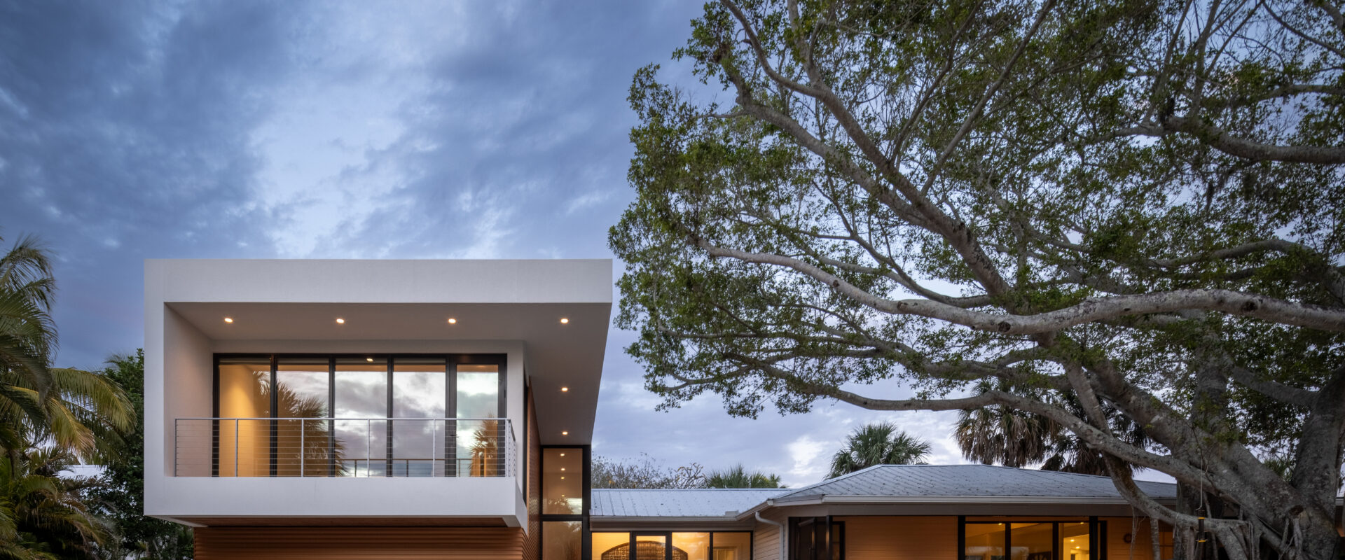 The modern addition and the original schoolhouse at dusk under oak limbs