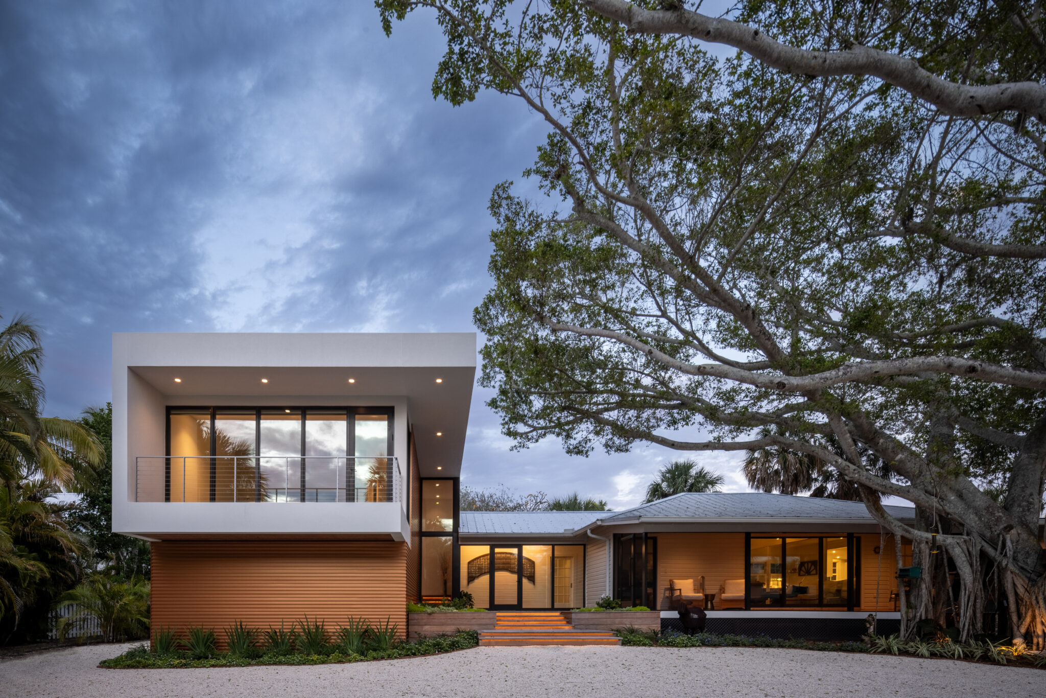 The modern addition and the original schoolhouse at dusk under oak limbs