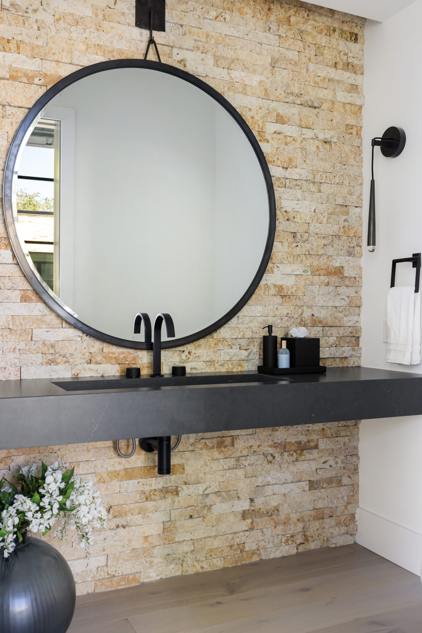 Powder room with a stone wall, floating black vanity and round mirror
