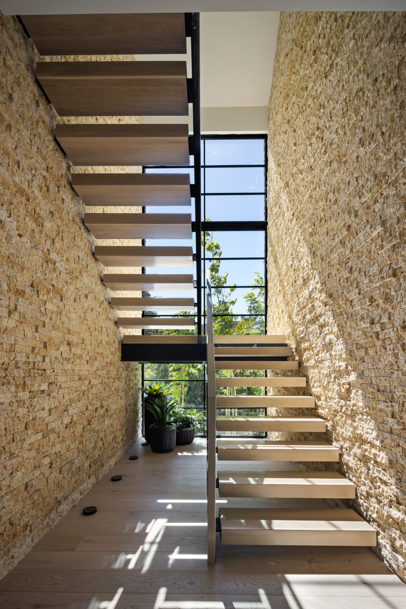 Floating wood stair beside a stacked stone wall