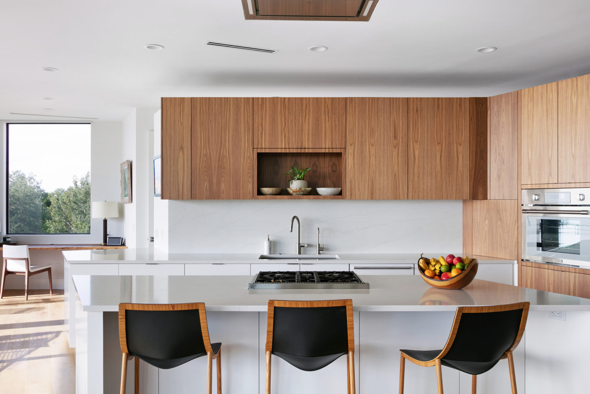 Kitchen with walnut cabinetry, white quartz island and black stools