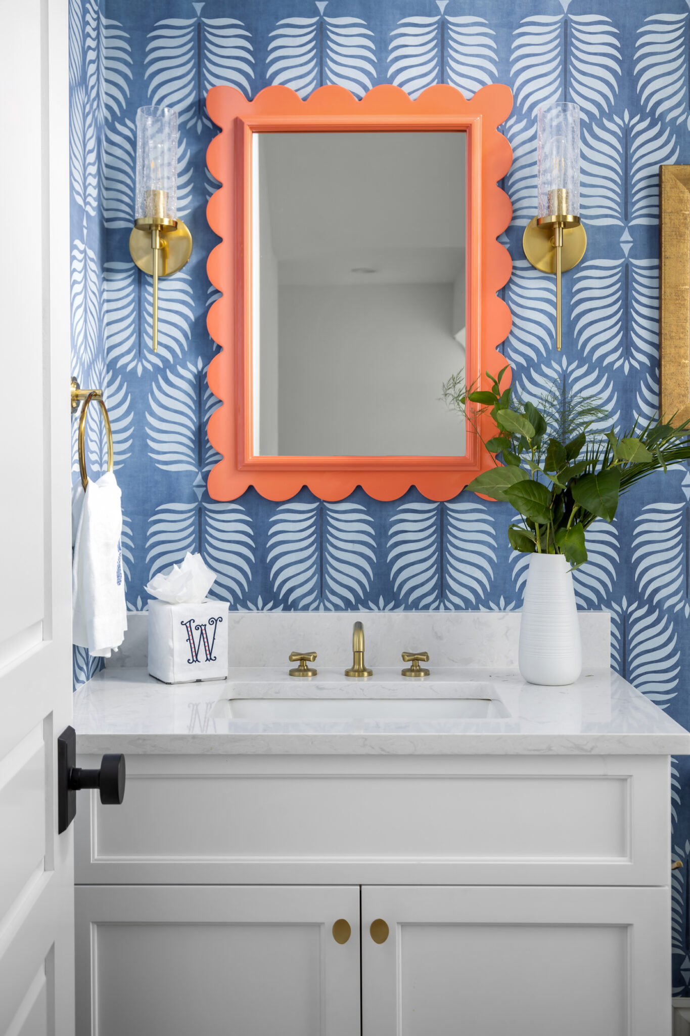 Powder room with blue patterned wallpaper and an orange scalloped mirror
