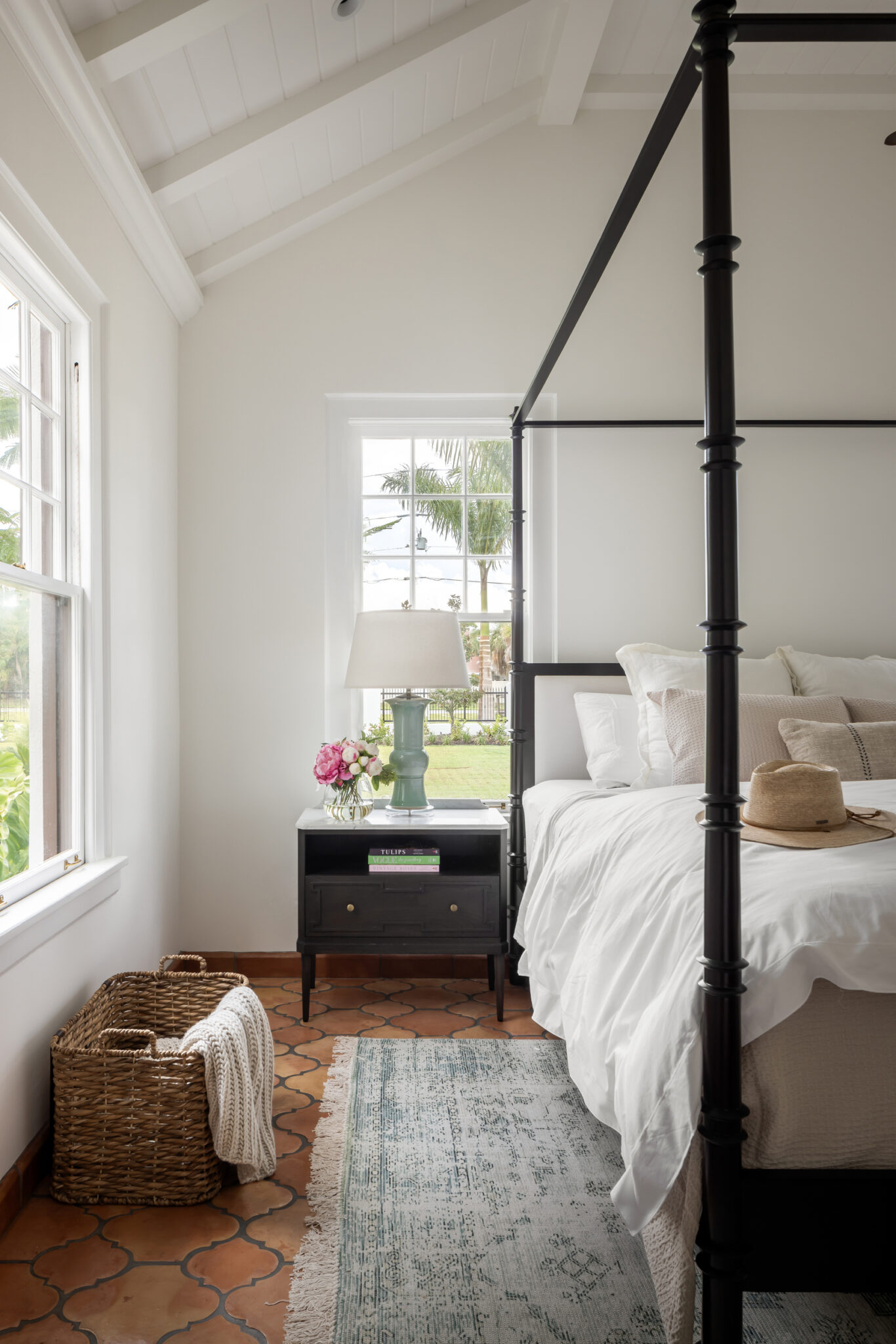 Four-poster bed beside a window with a woven basket