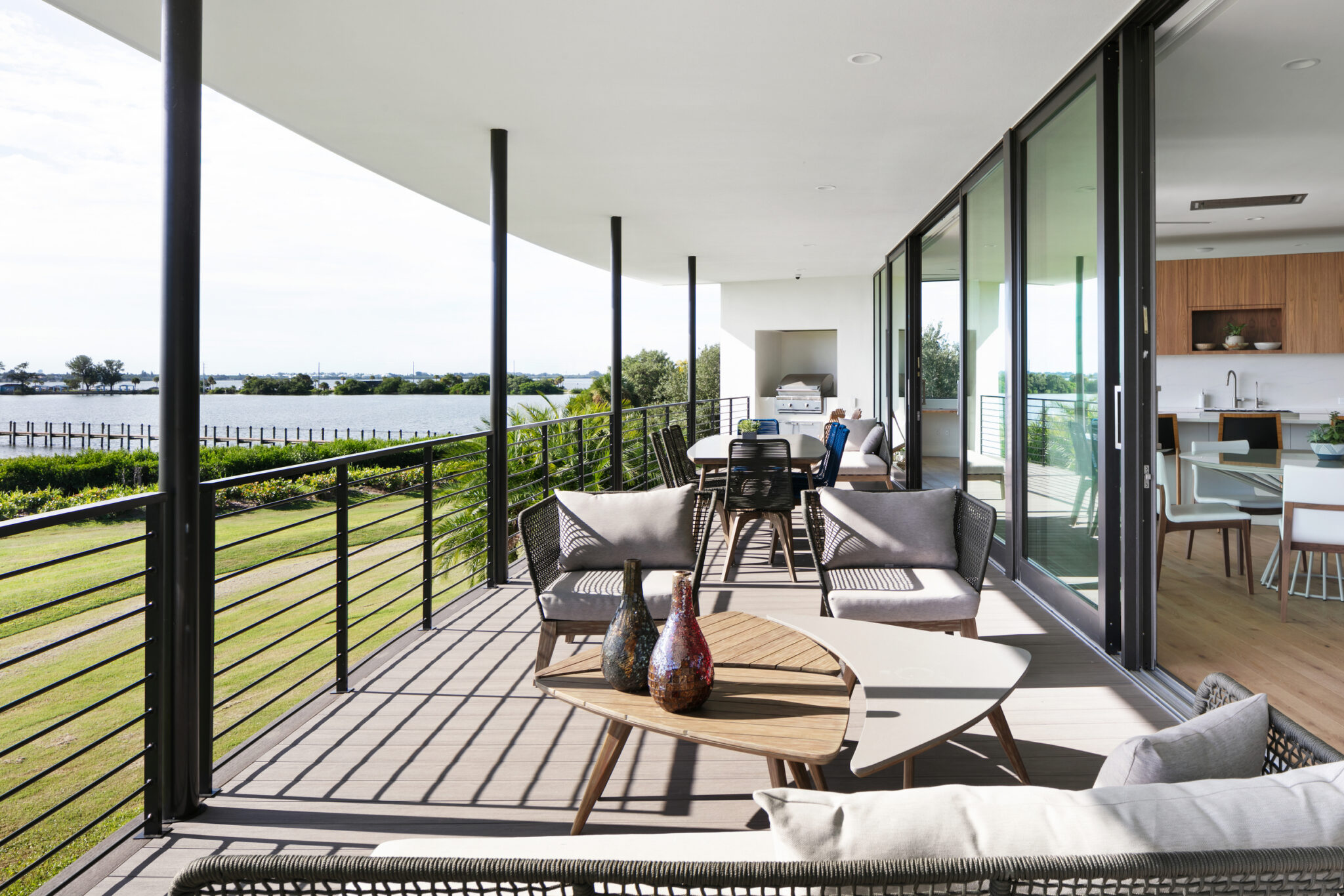 Covered balcony seating along a wall of glass above the lawn