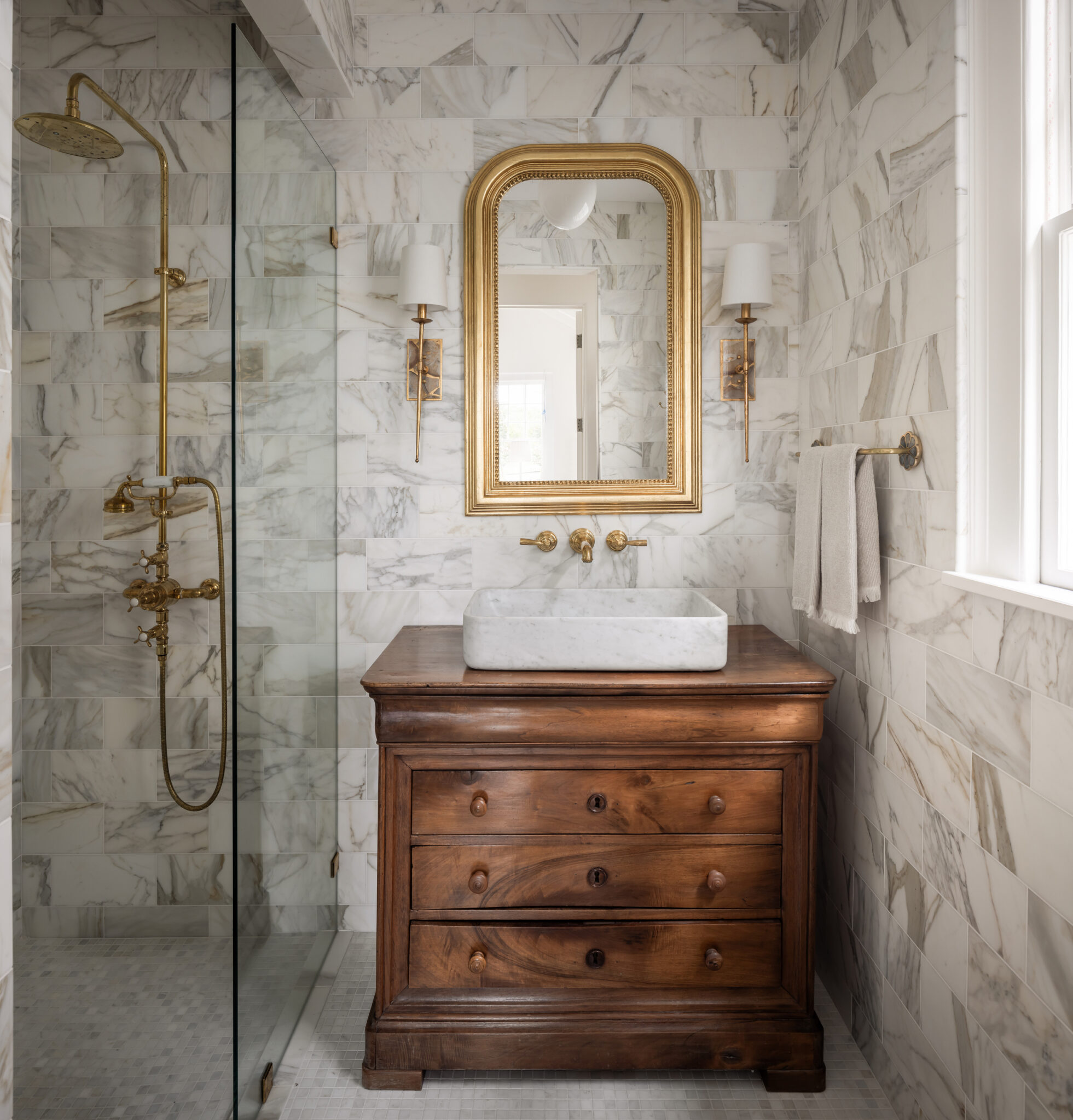 Marble shower and an antique wood vanity with a brass mirror