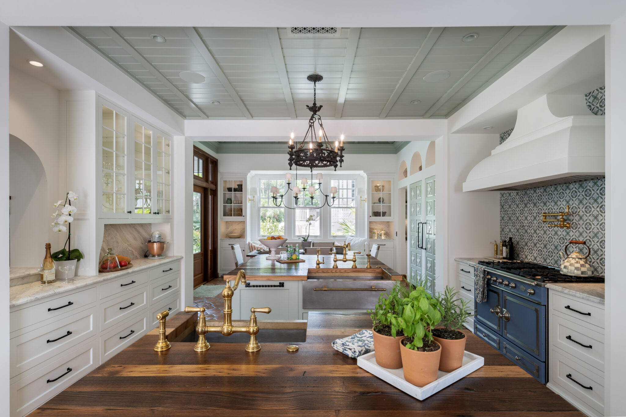 Kitchen island with a brass faucet and herbs, blue range beyond