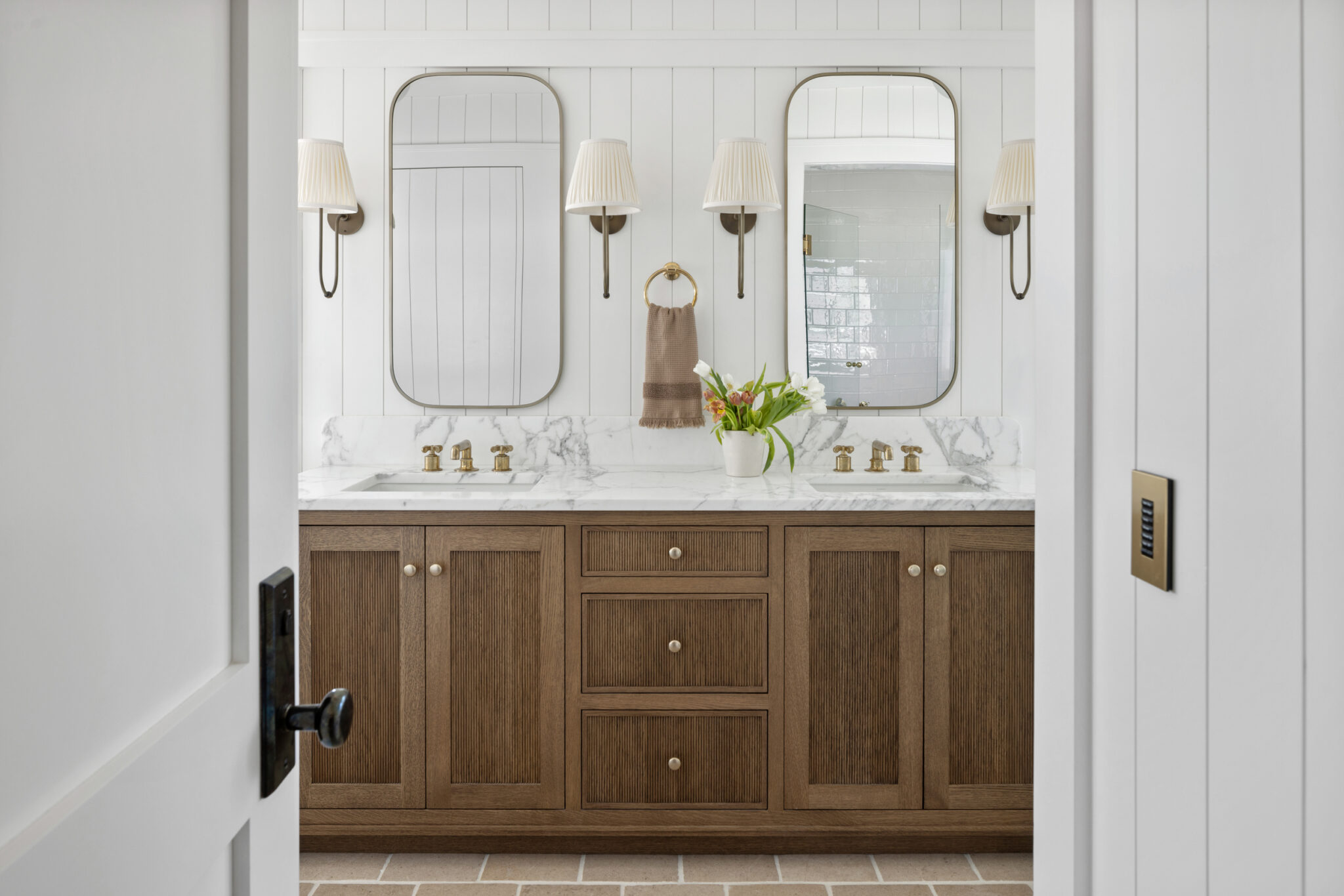 Double vanity in warm wood with arched mirrors and brass sconces