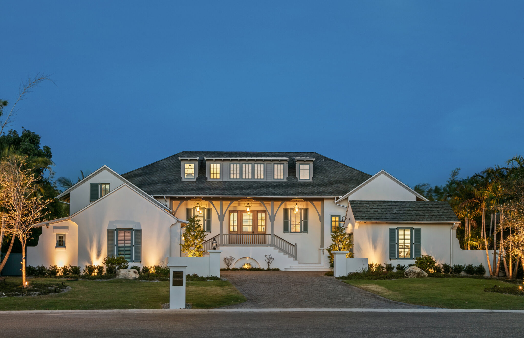 Blue Heron at dusk, a white coastal home with dormers and lit landscaping