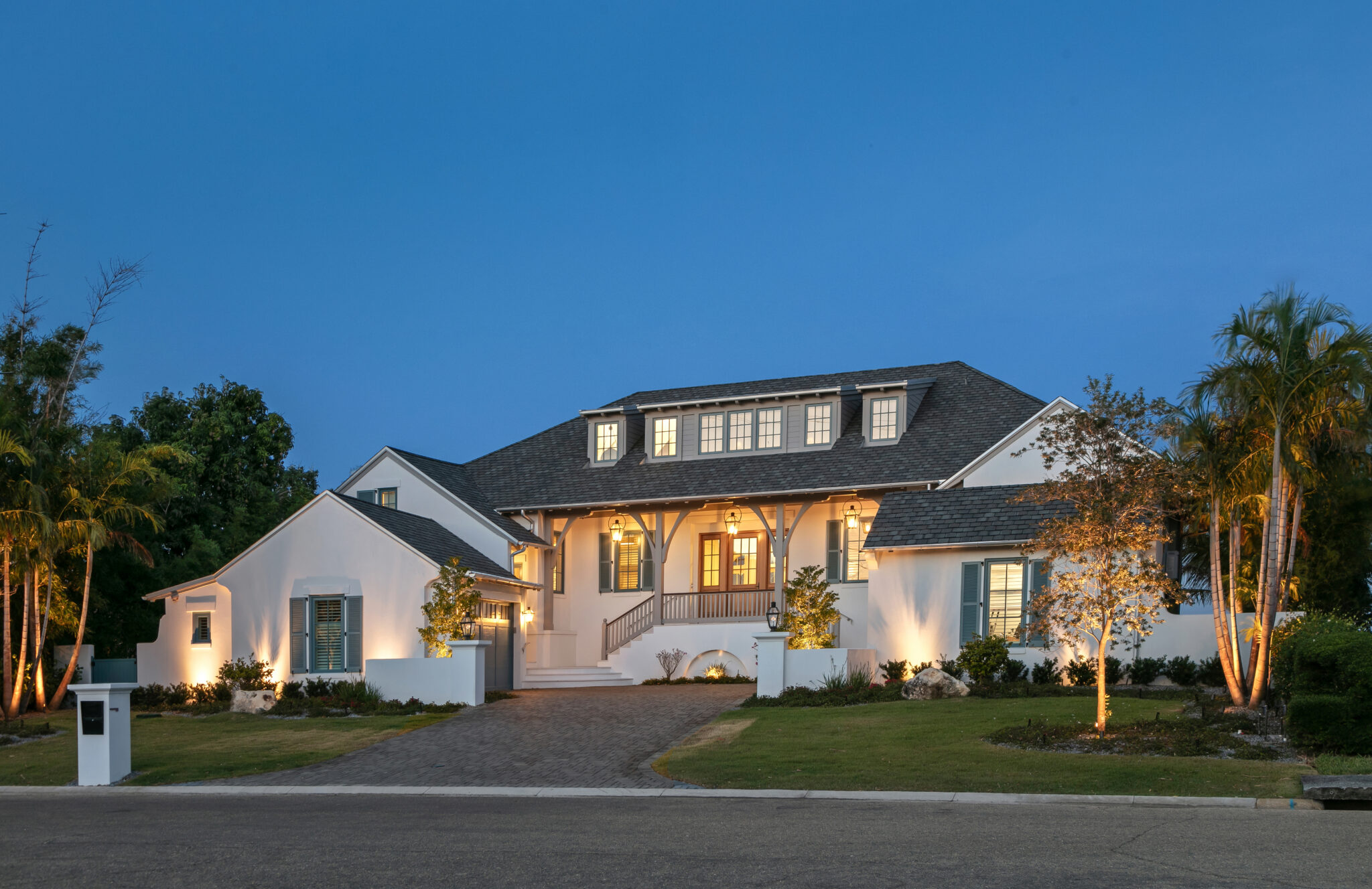 Front of Blue Heron at dusk with a paver drive and palms