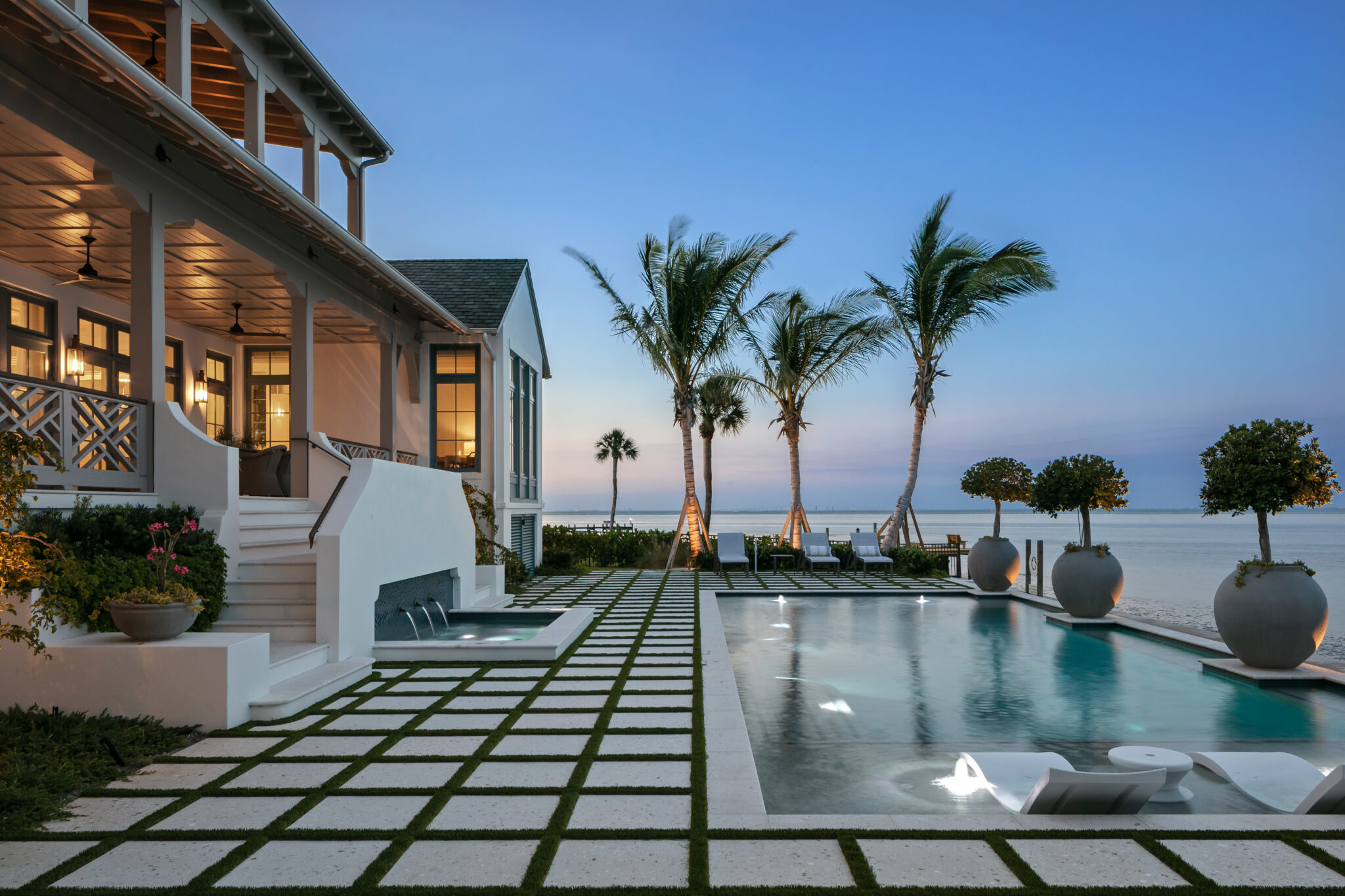 Pool set in a grid of pavers and turf, with palms and open water beyond