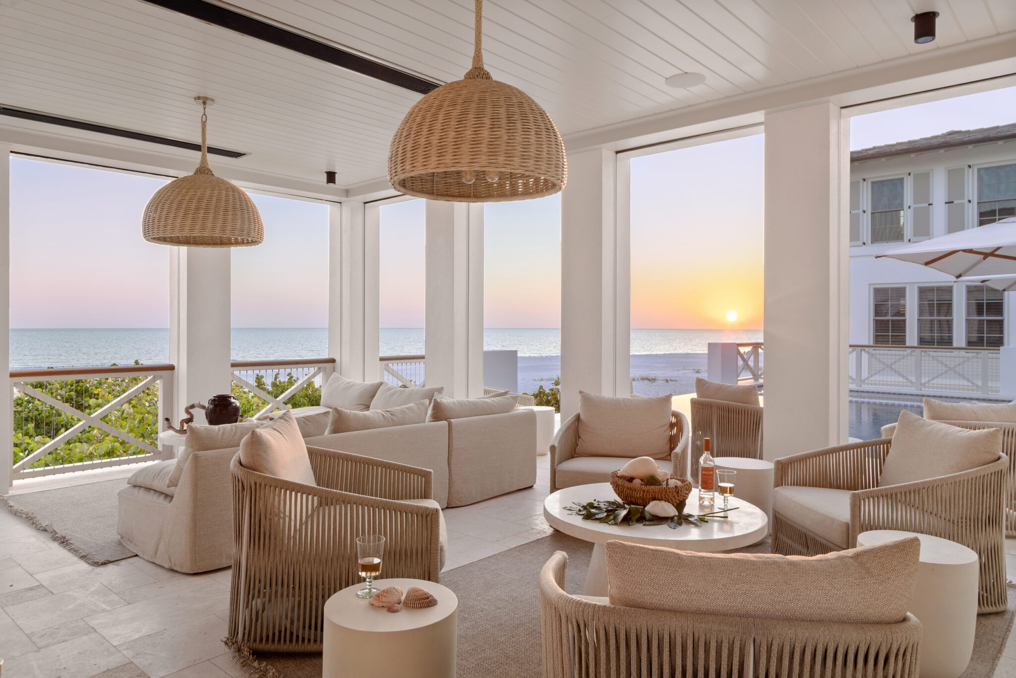 Covered porch living room with woven chairs at sunset over the Gulf