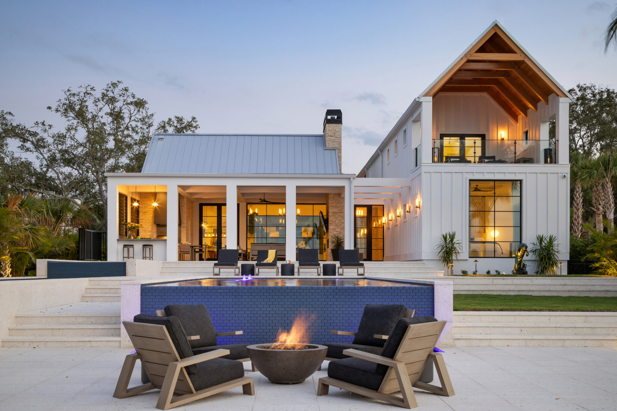 Fire pit and chairs on the pool terrace with the house lit behind