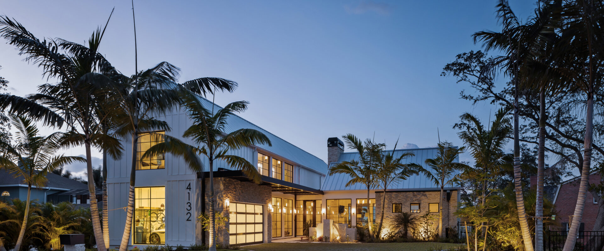Motor court and front of Modern River House lit at dusk under palms