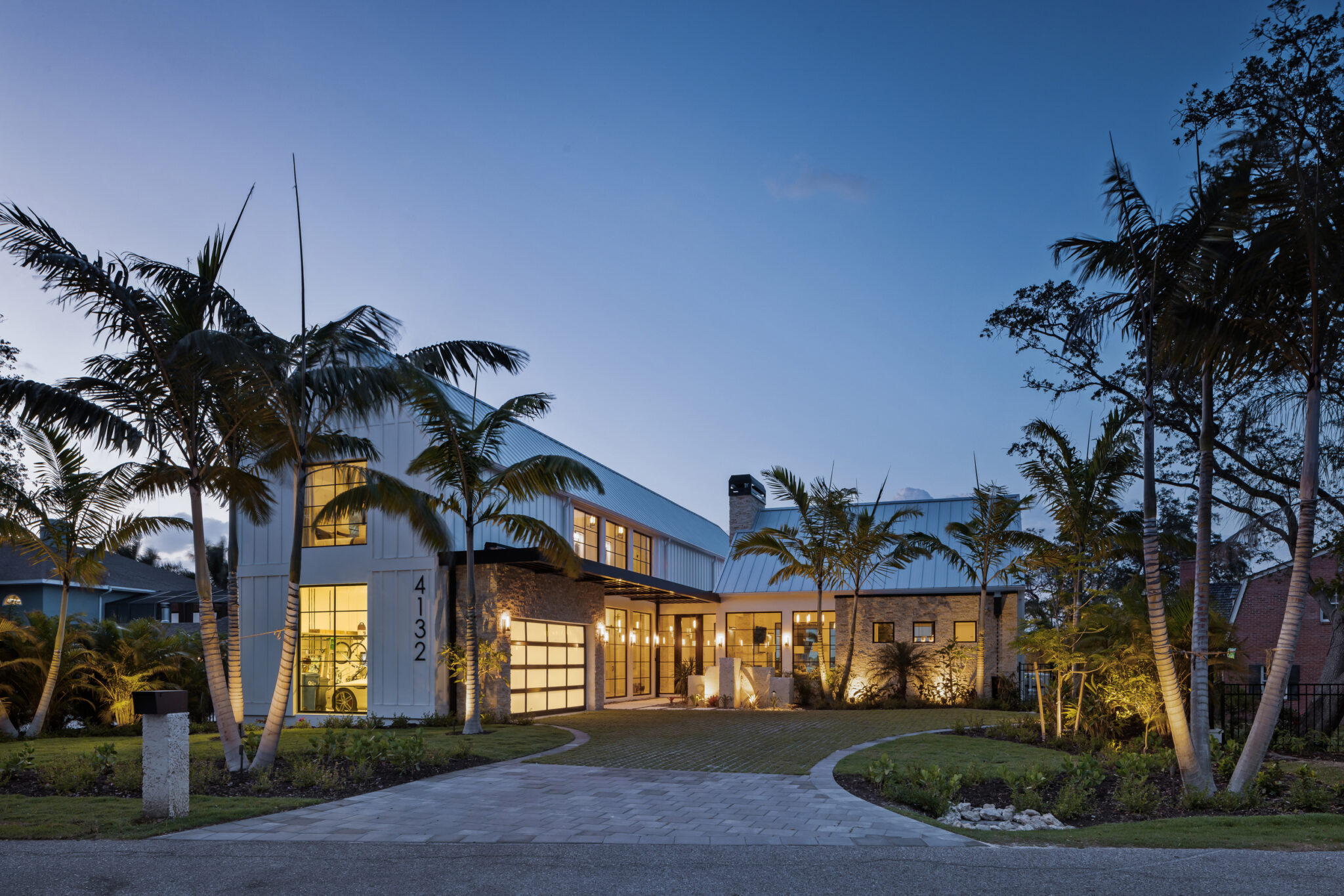 Motor court and front of Modern River House lit at dusk under palms