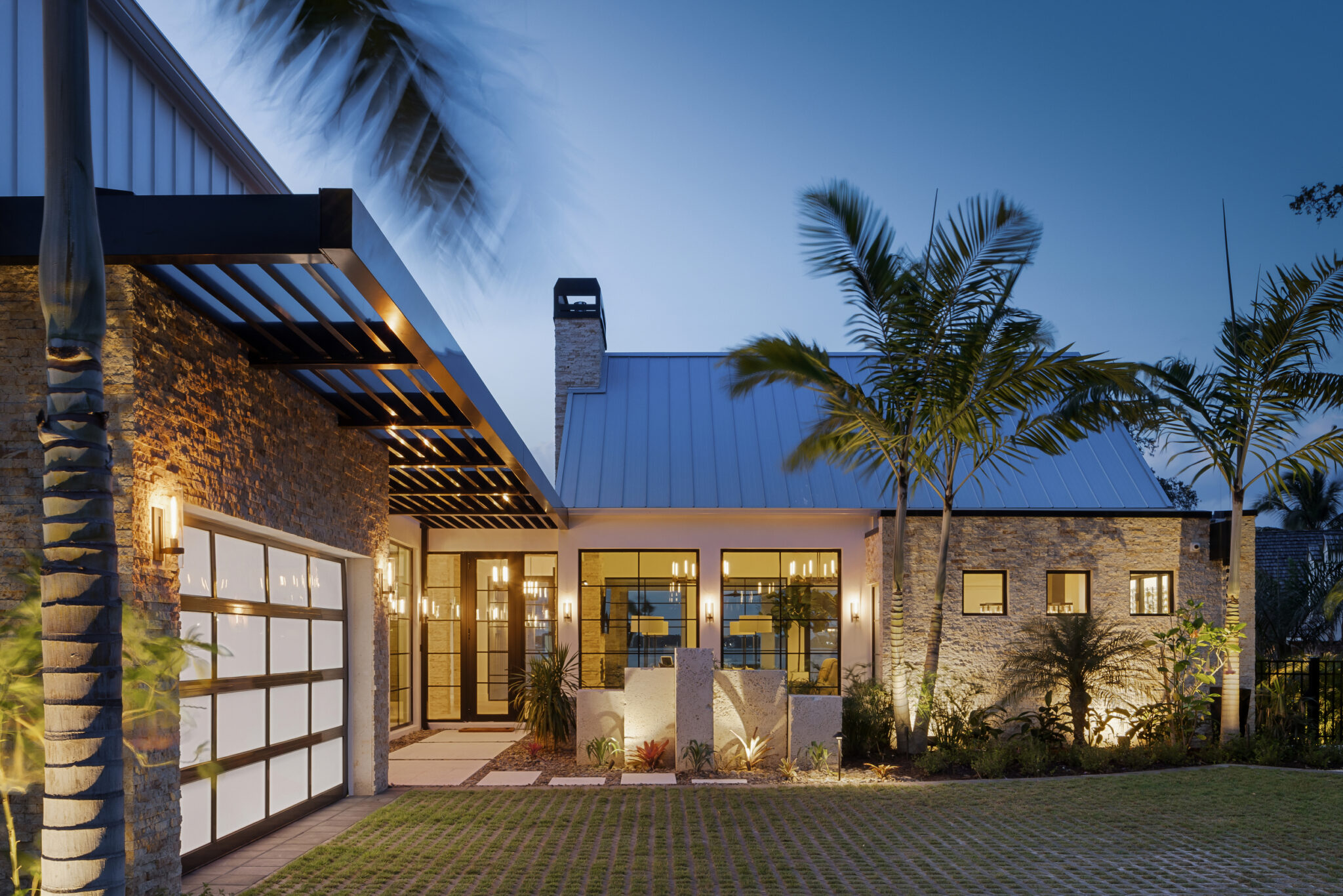 Modern River House at dusk, with stone walls, a metal roof and a glass garage door
