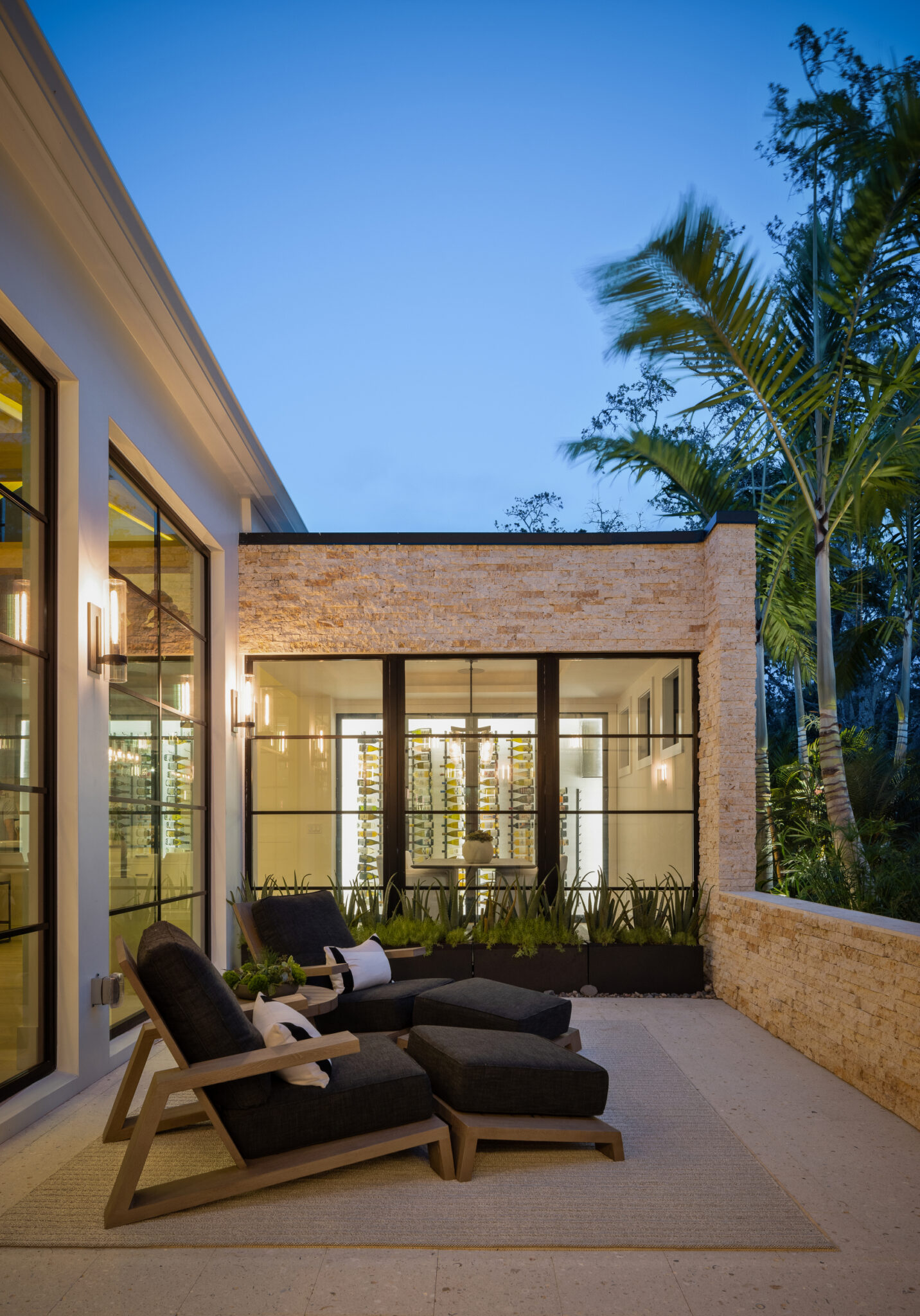 Stone courtyard wall and lounge chairs beside floor-to-ceiling glass