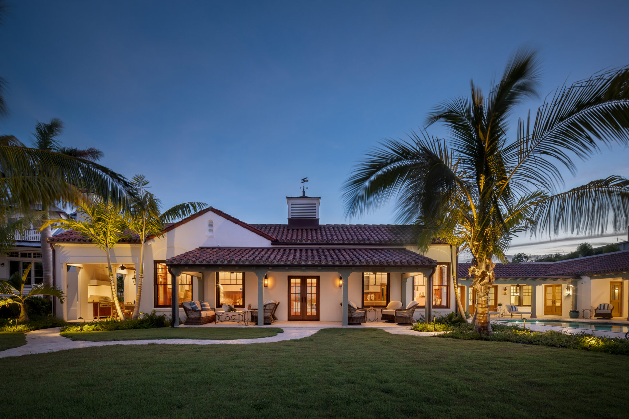 Barrel-tile roofs and white stucco of the estate behind palms at dusk