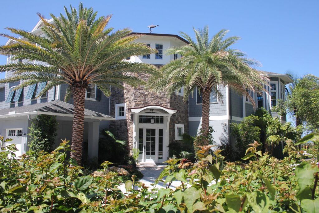 Shingle-sided beachfront home in Holmes Beach with a stone entry tower and palms, completed by Ross Built in 2017