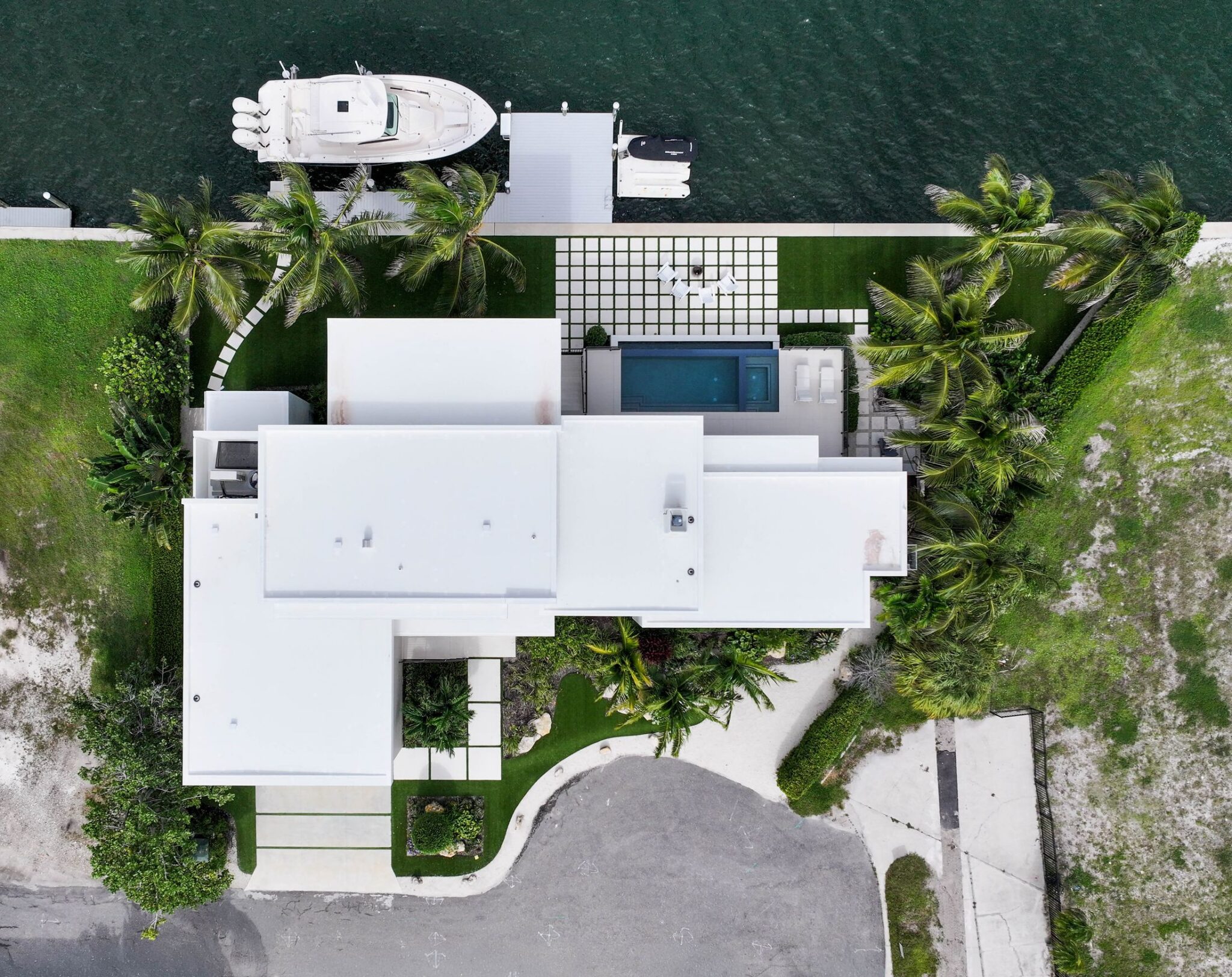 Aerial view looking down on Bayview Residence, with its flat roofs, pool, lawn pavers and dock on the bay