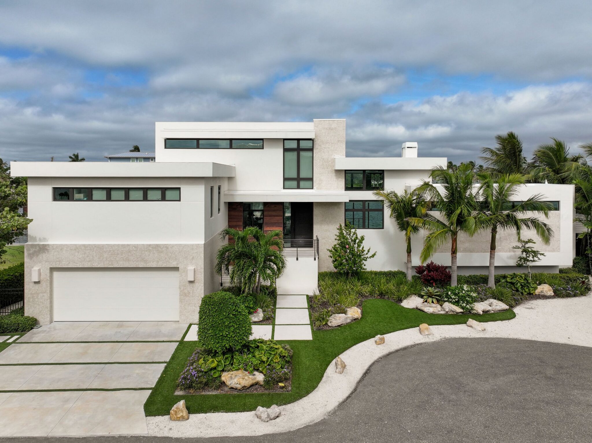 Front elevation of Bayview Residence with a stone-clad garage wing, wood entry and tropical landscaping
