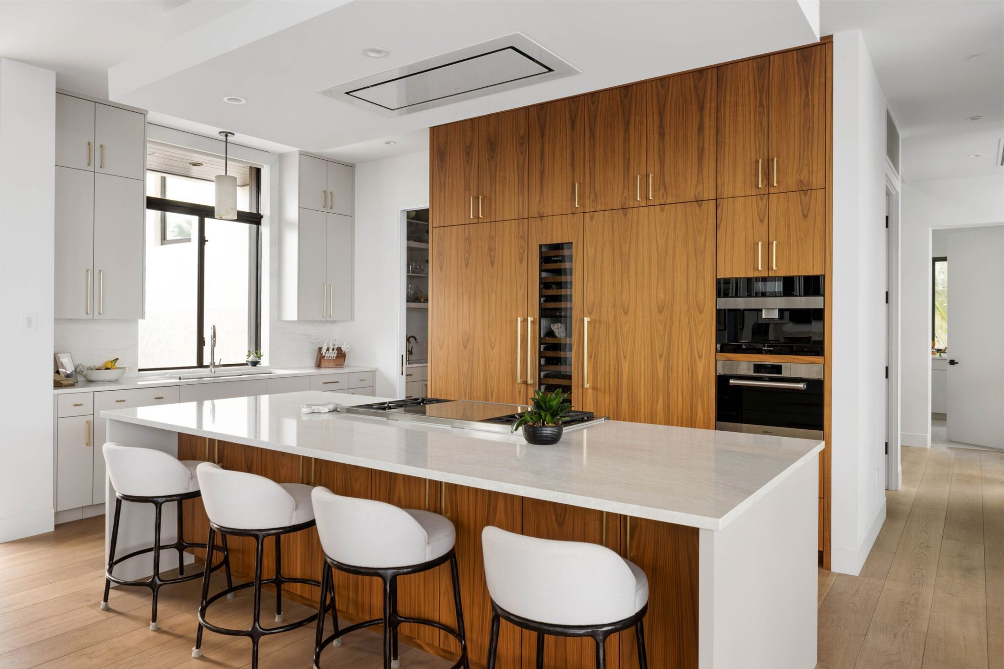 Kitchen with a wall of walnut cabinetry, a white island with seating and a ceiling hood