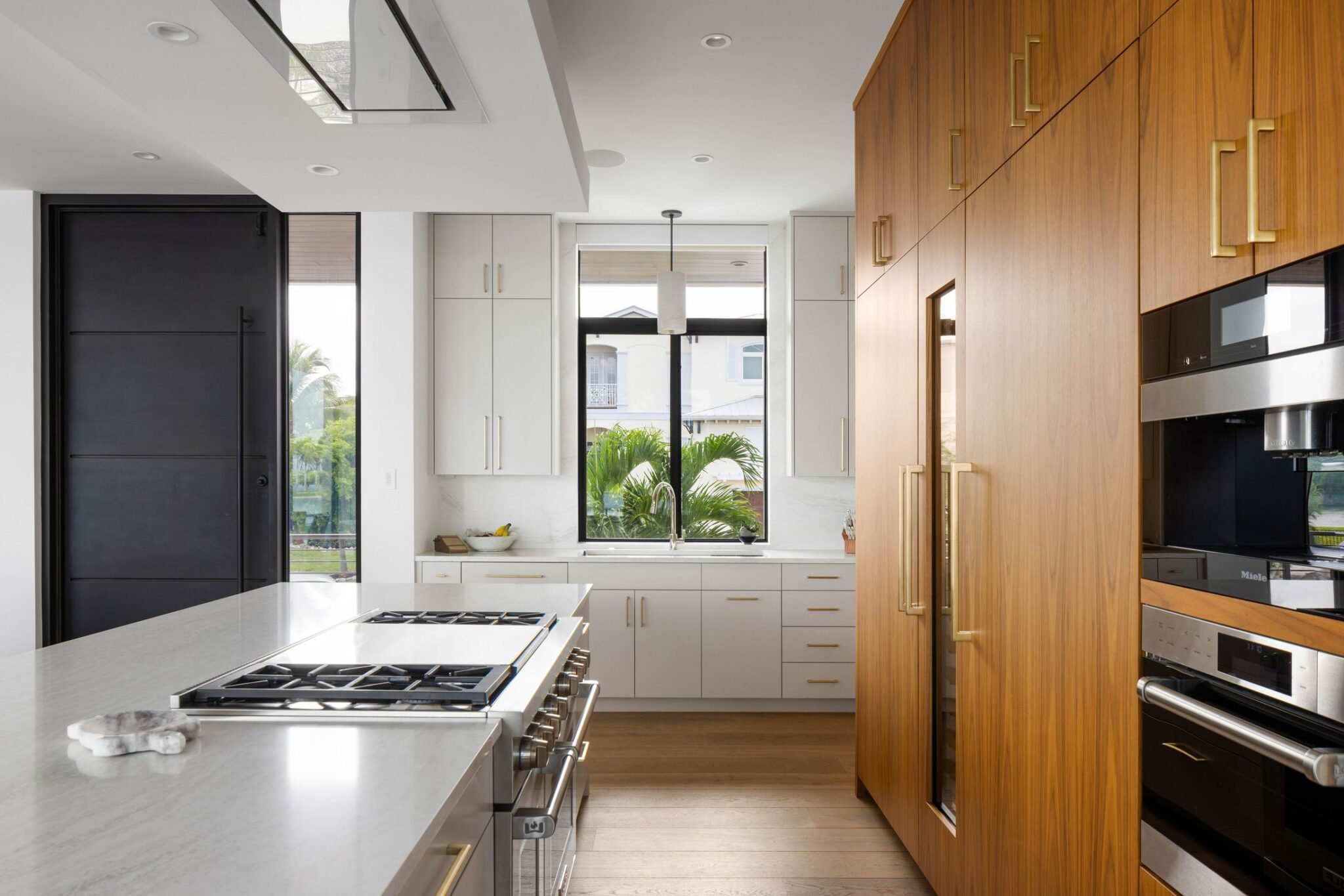 Kitchen looking toward the entry door, with a cooktop in the island and built-in ovens