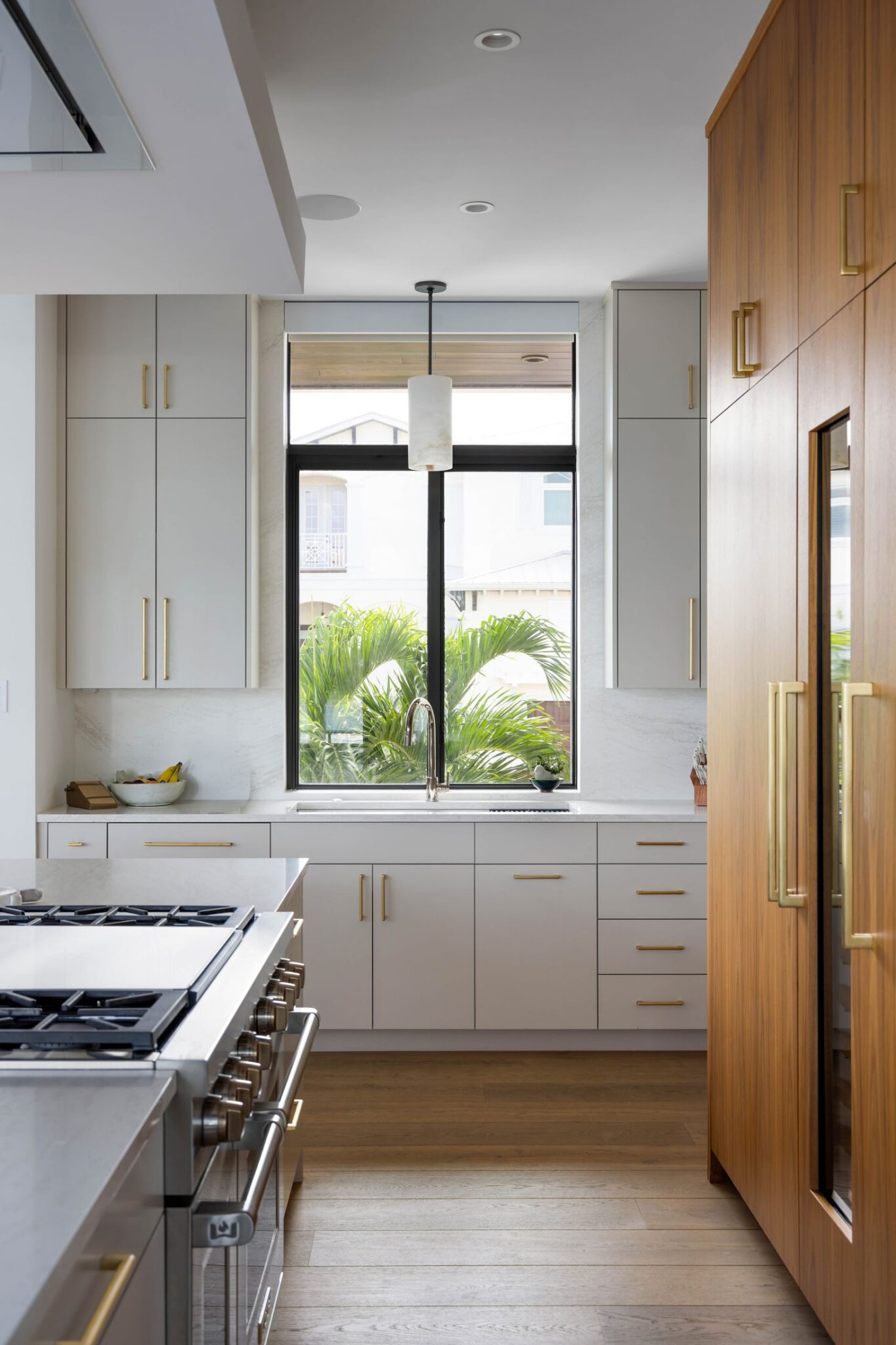 Kitchen sink wall with painted cabinetry, brass hardware and a window to the garden