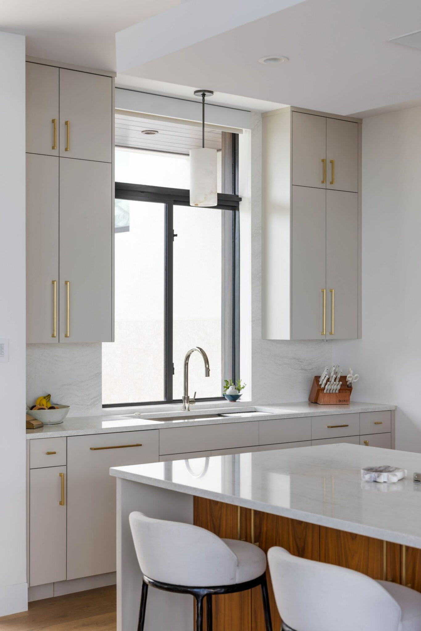 Kitchen window wall with painted upper cabinets and brass pulls