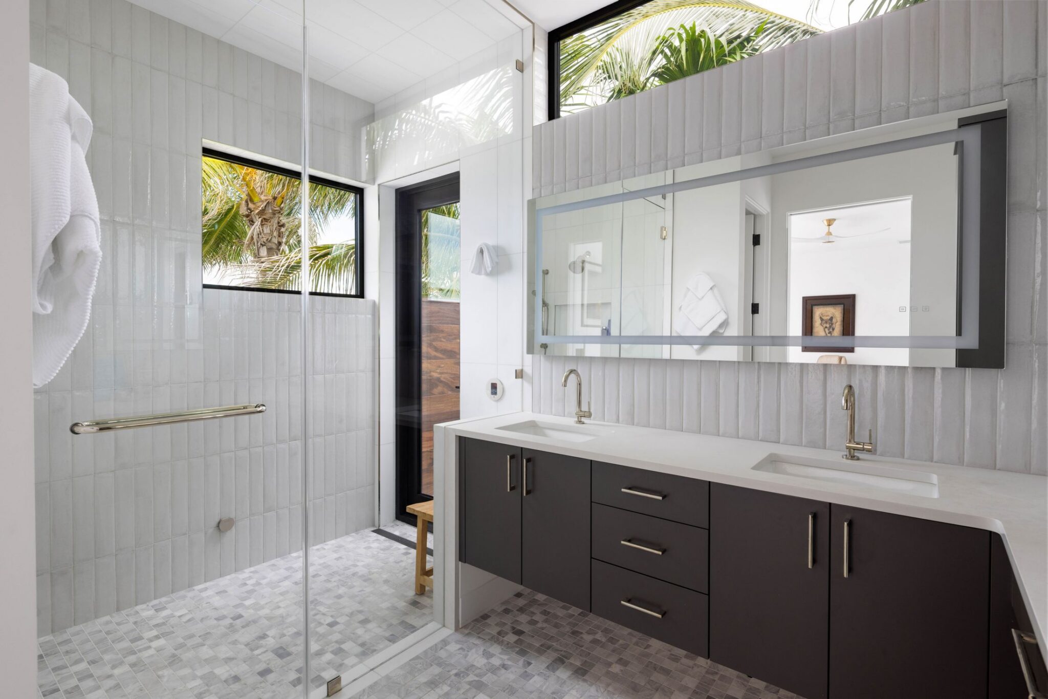 Bathroom with a double vanity, lit mirror and frameless glass shower