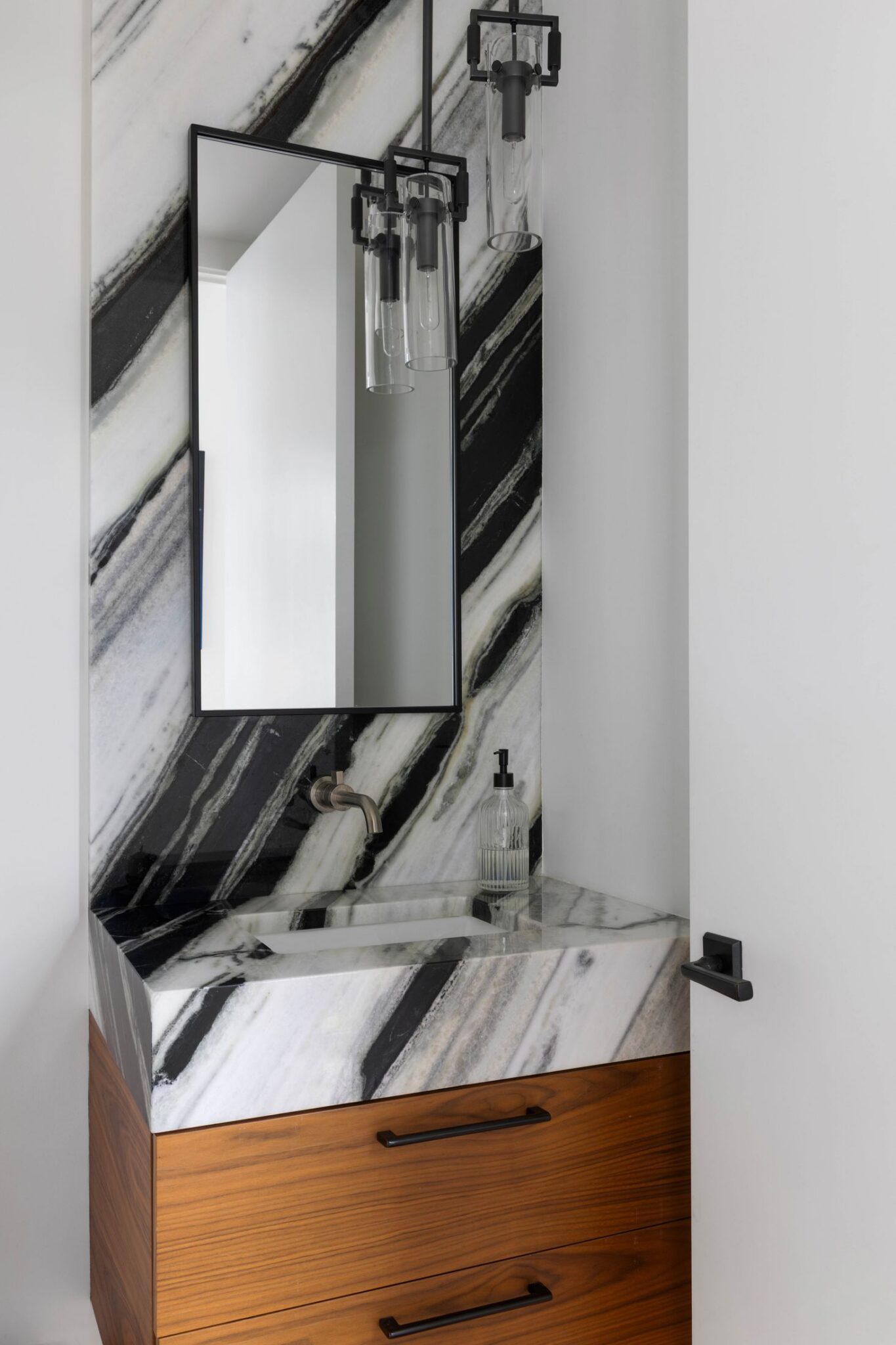 Powder room with a book-matched black and white stone wall and floating mirror
