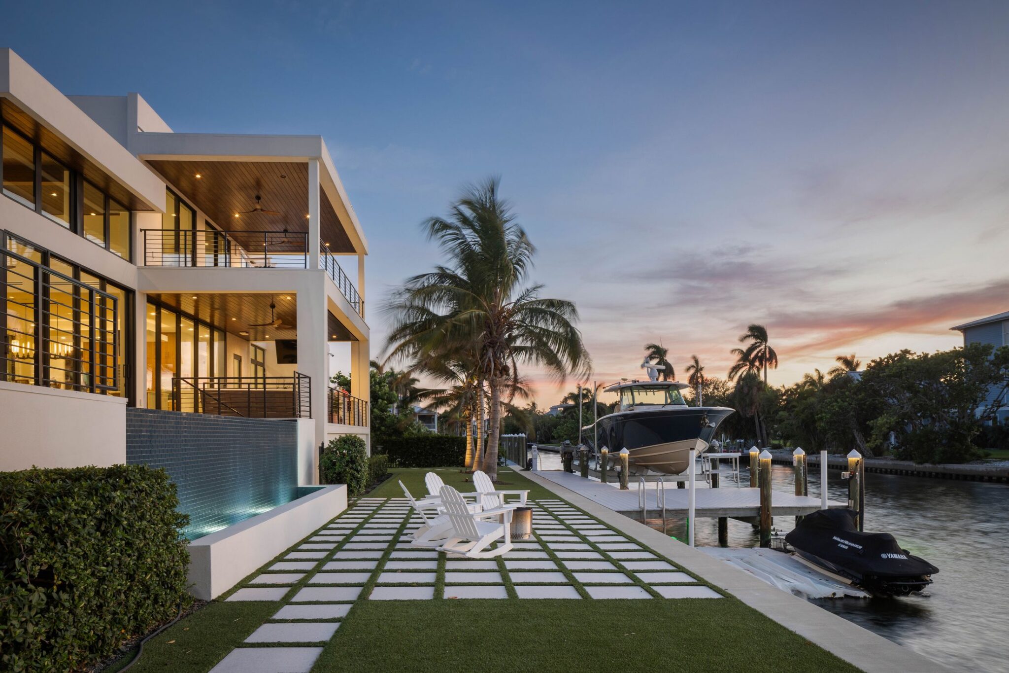 Bay side of the home at dusk with lit interiors, pool water wall and dock