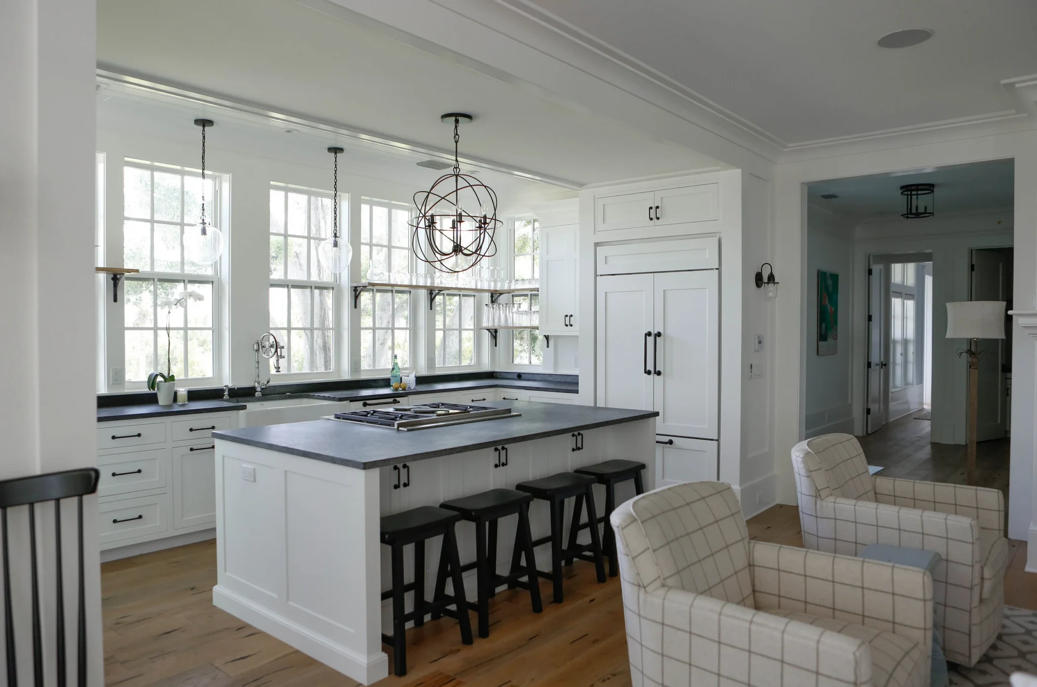 Bright kitchen with white cabinetry, black countertops, large windows, hanging glass light fixtures, and a kitchen island with black stools