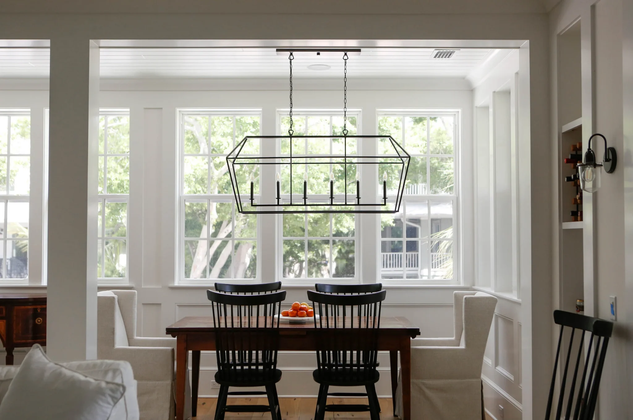 Dining room with a wooden table, black and beige chairs, a modern geometric chandelier, and large windows with trees outside