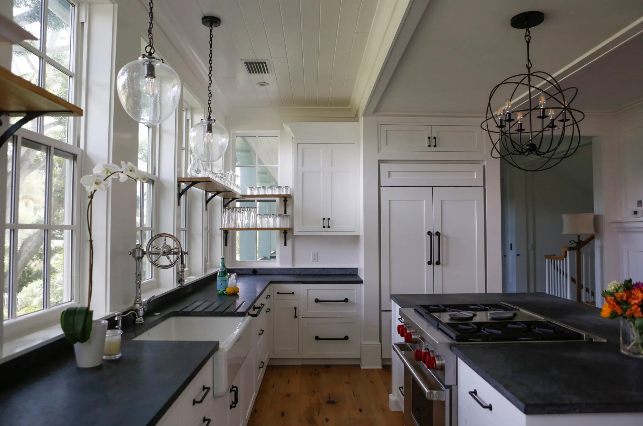 Bright kitchen with white cabinets, black countertops, large windows, modern light fixtures, and a gas stove
