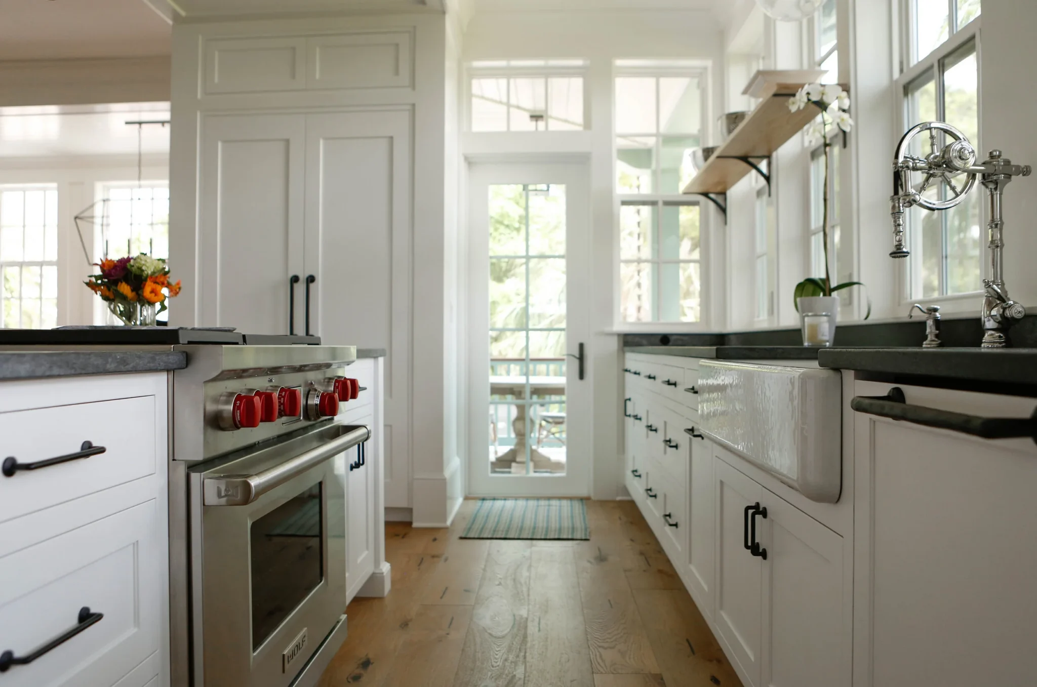 A modern kitchen with white cabinets, a stove with red knobs, black countertops, a farmhouse sink