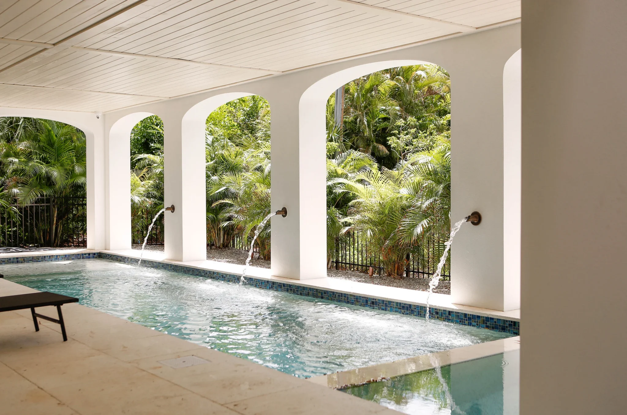 Covered outdoor pool with water features, white arches, overlooking lush green tropical plants