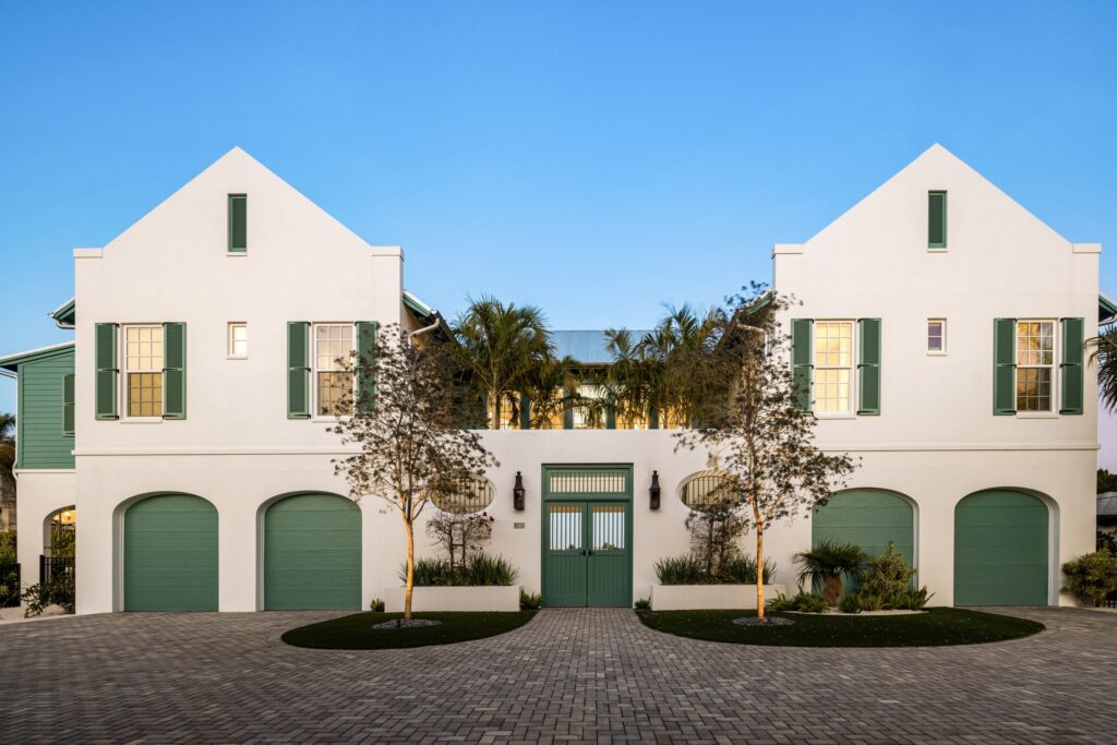 Bimini Bay House, a white stucco Ross Built home in Anna Maria with twin gables and green shutters and doors, at dusk
