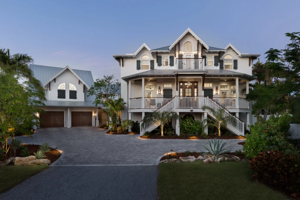 Large white multi-story house with dark green shutters, a steep metal roof, and a front porch with stairs