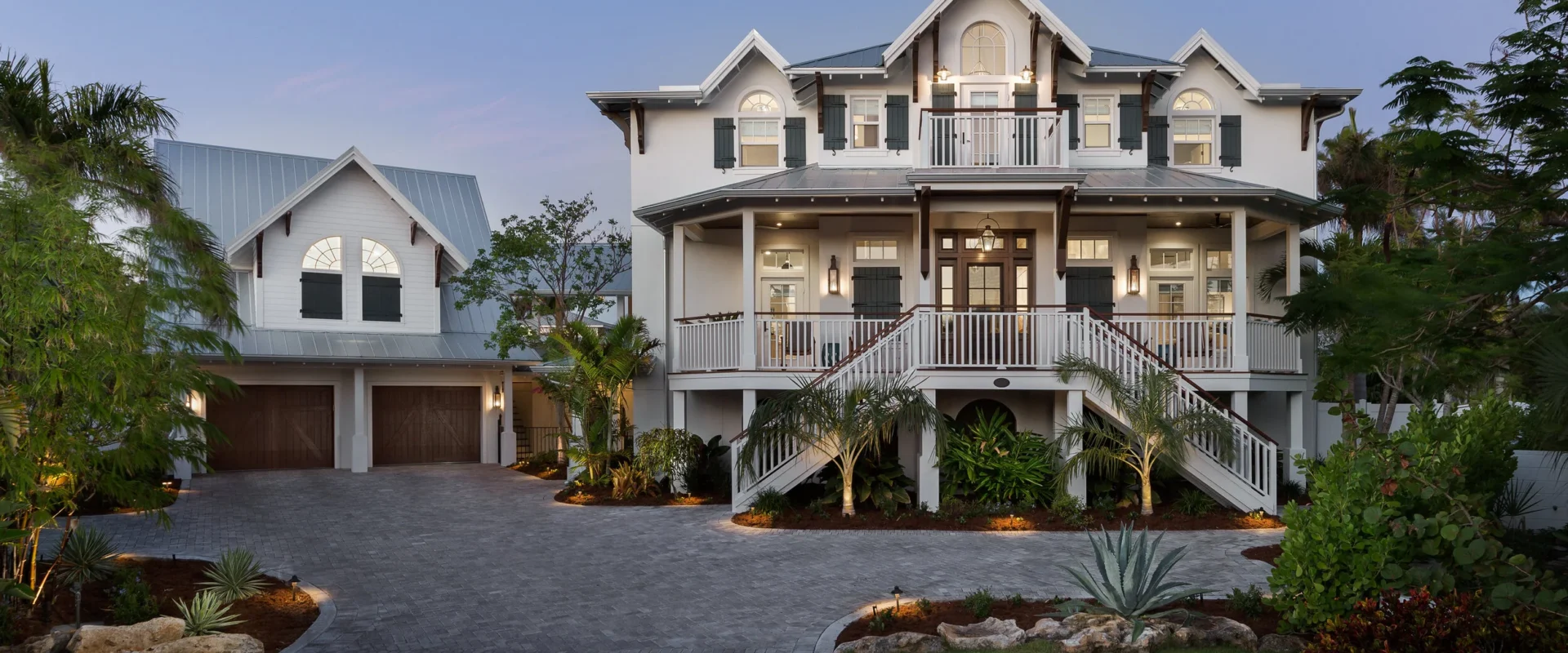 Large white multi-story house with dark green shutters, a steep metal roof, and a front porch with stairs