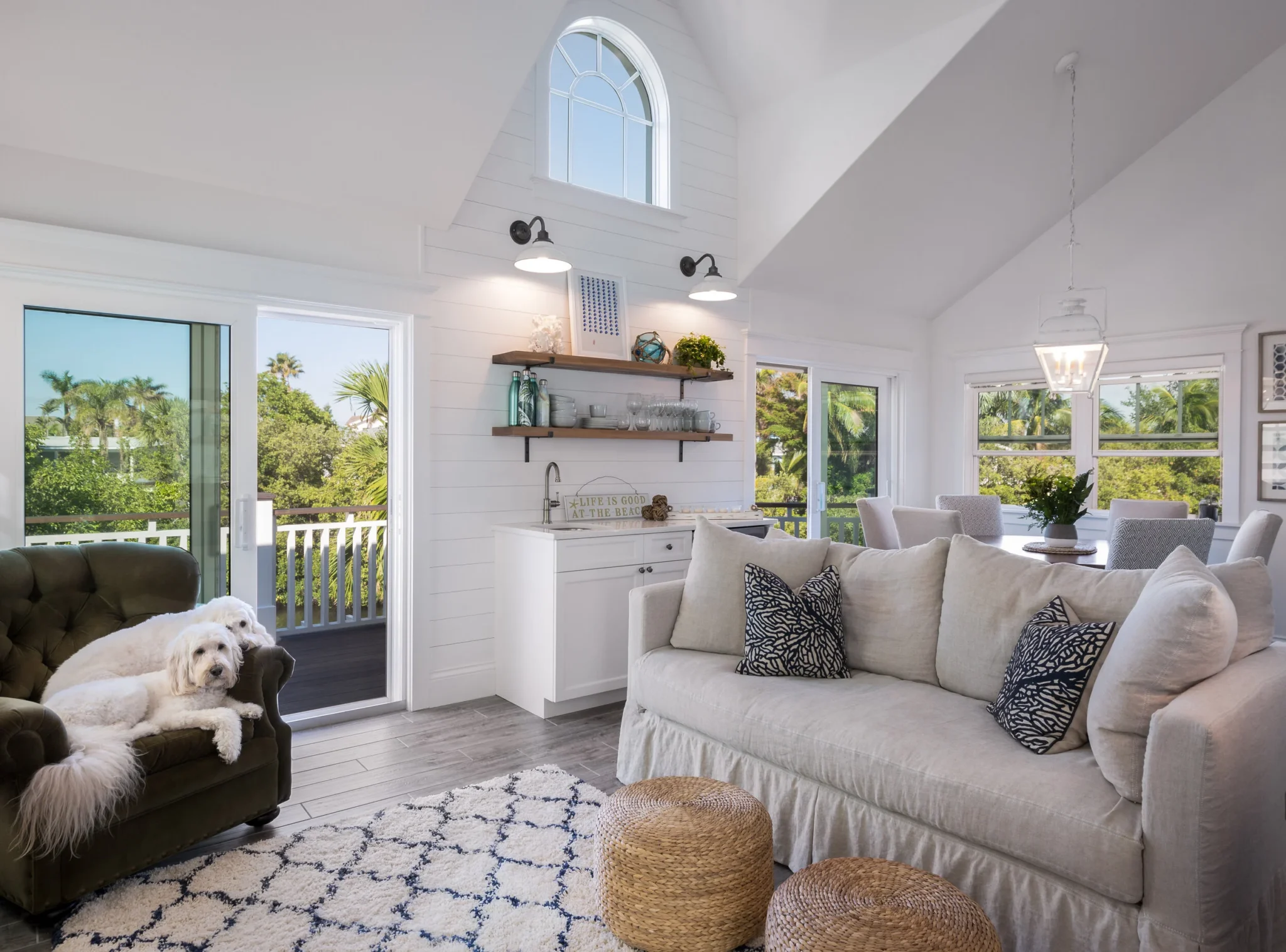 Bright living room with white walls, a white sofa with black and white throw pillows, two woven ottomans